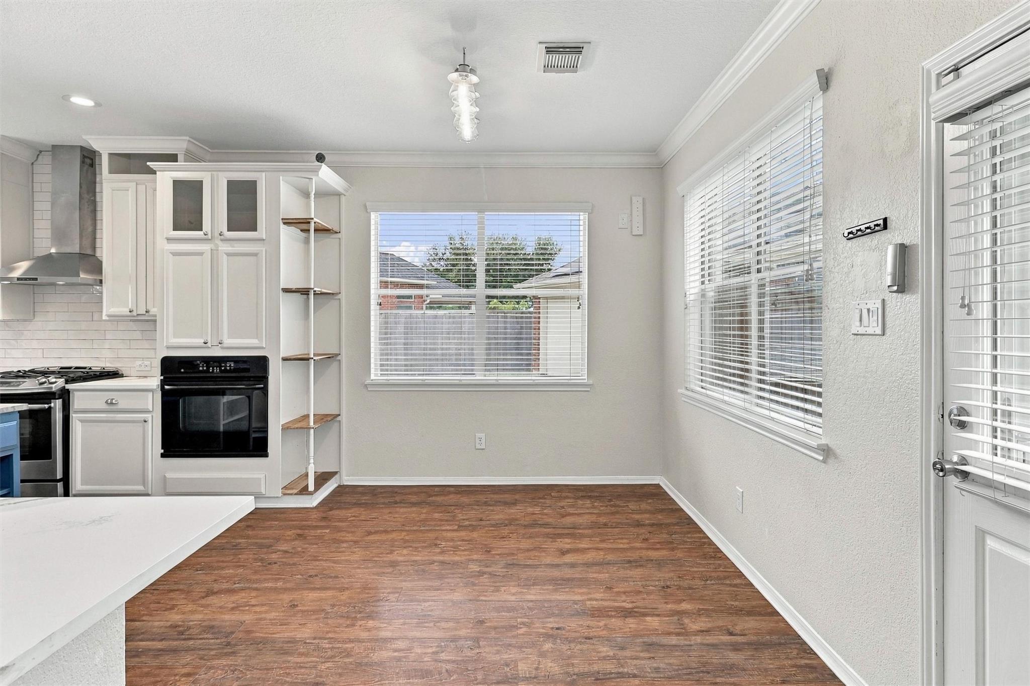 Vacant kitchen and dining area with white cabinets, wood-look floors, and large windows with blinds.