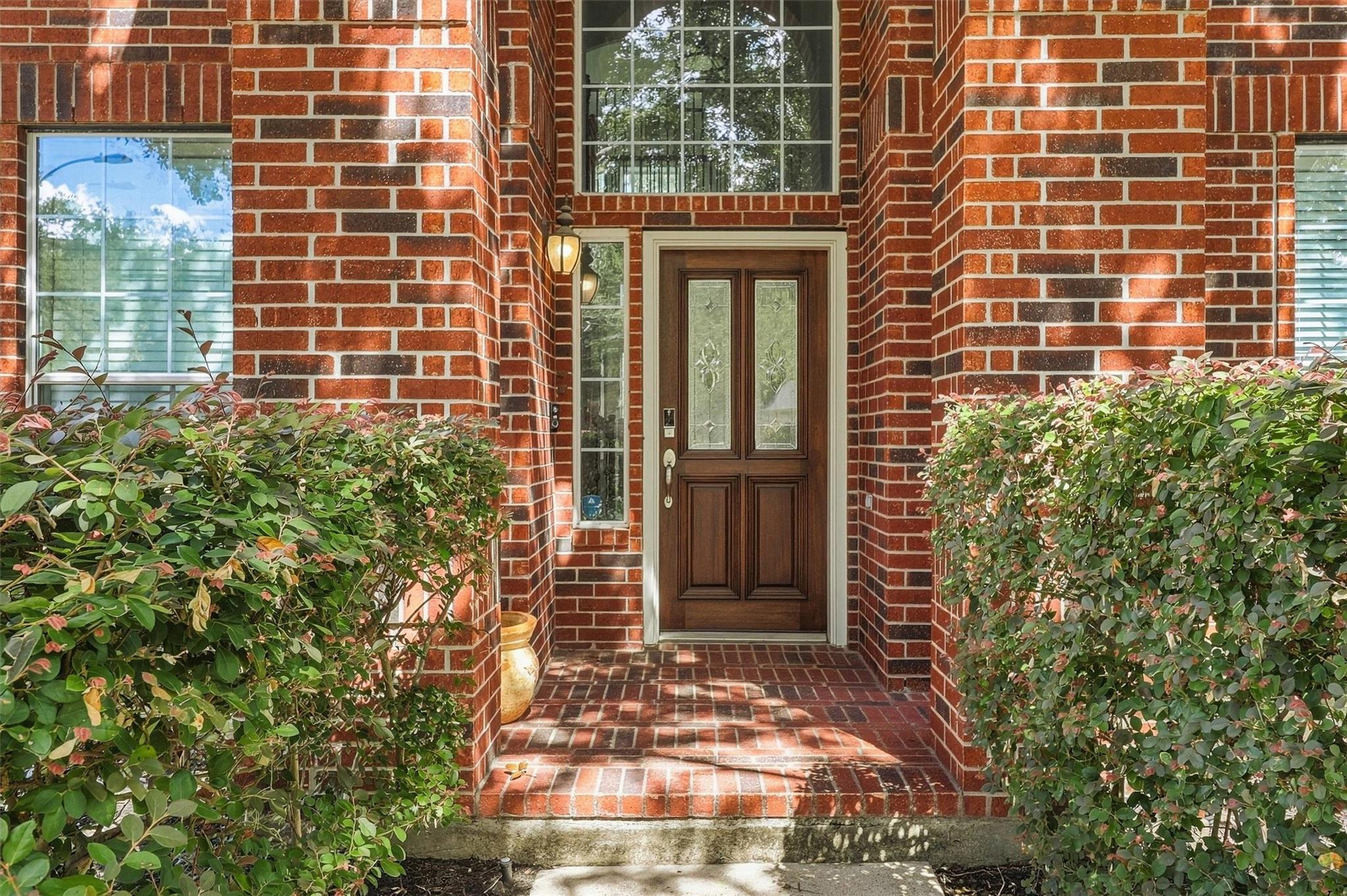 Recessed red brick entry with a dark wood front door, tall windows, and leafy shrubs.