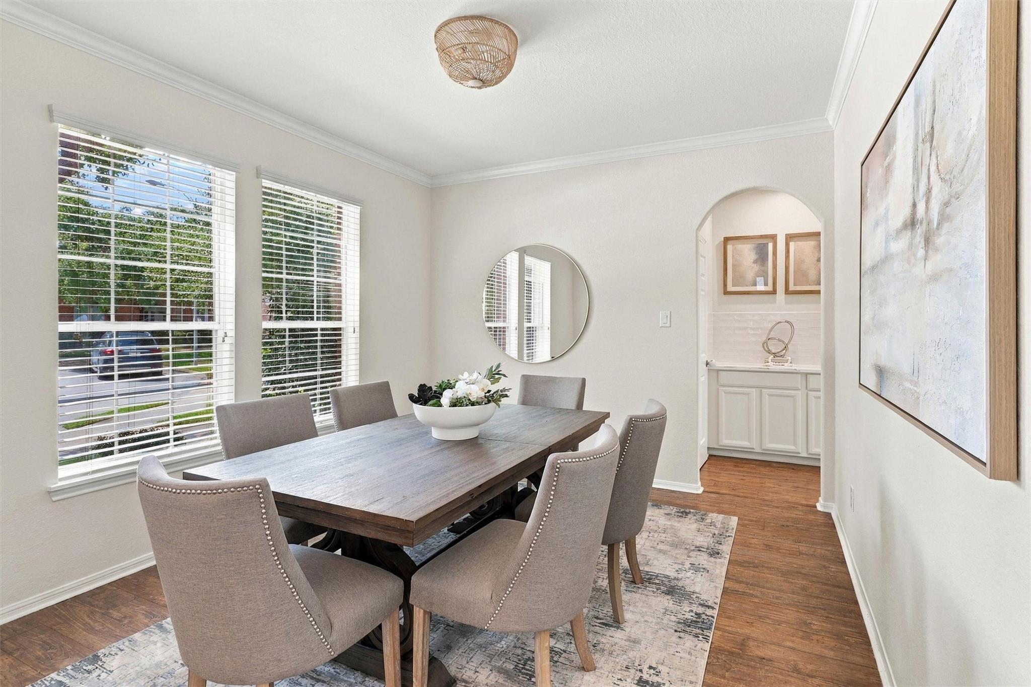 Dining room with a wood table, upholstered chairs, bright windows, and an arched cabinet nook.
