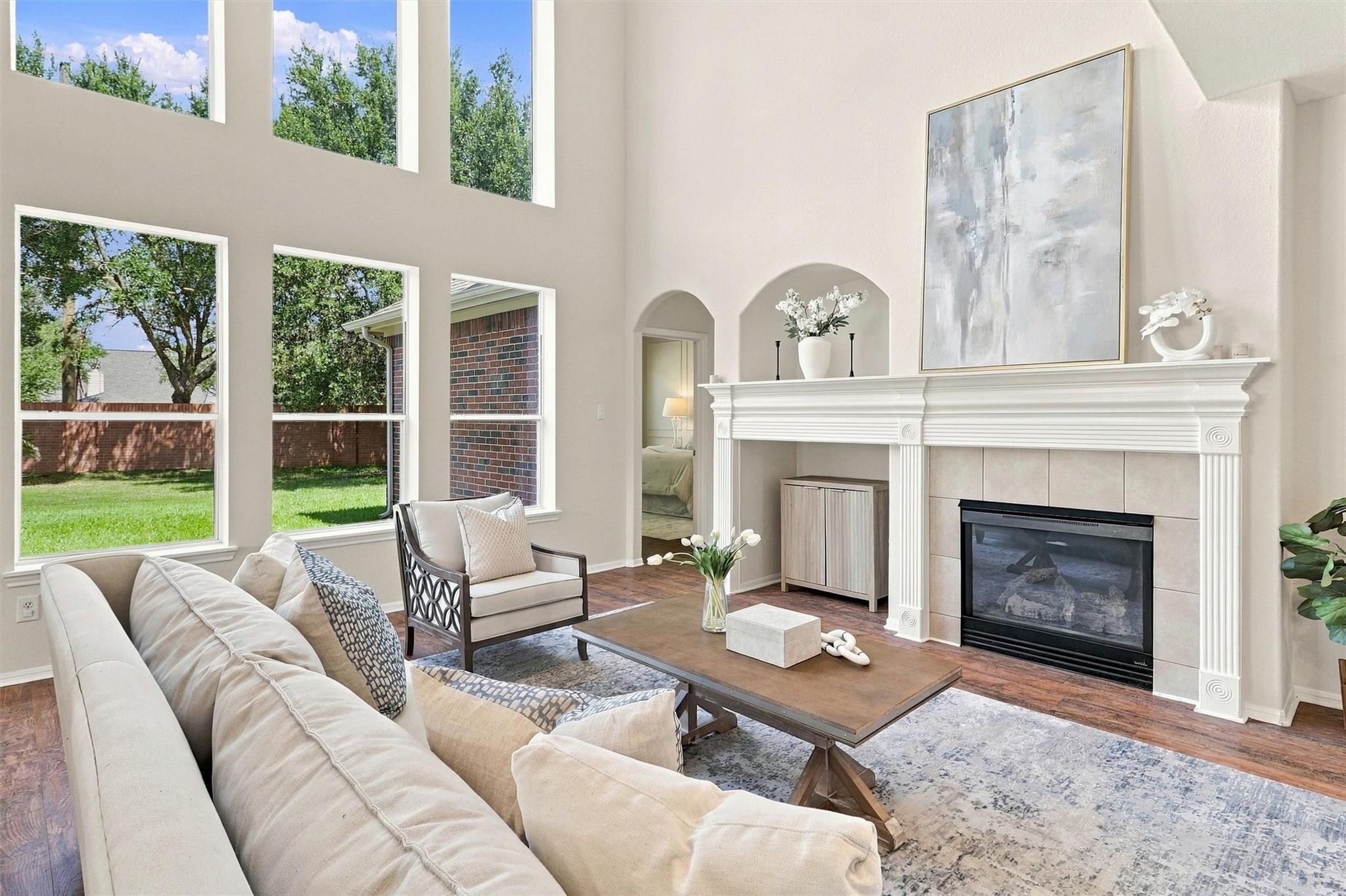 Two-story living room with tall windows, cream seating, and a white fireplace