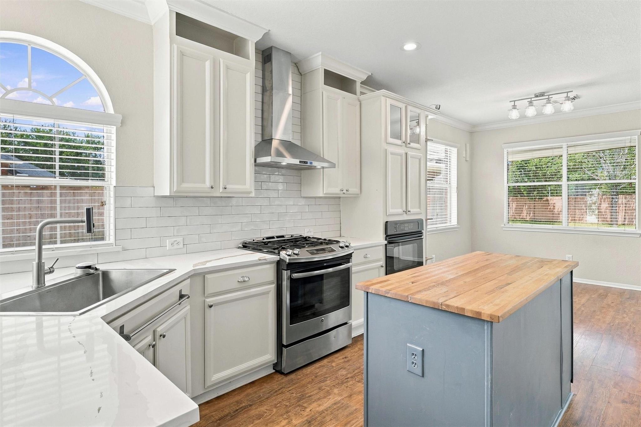 Kitchen with a butcher-block island, white cabinetry, stainless steel range, and arched window above the sink.