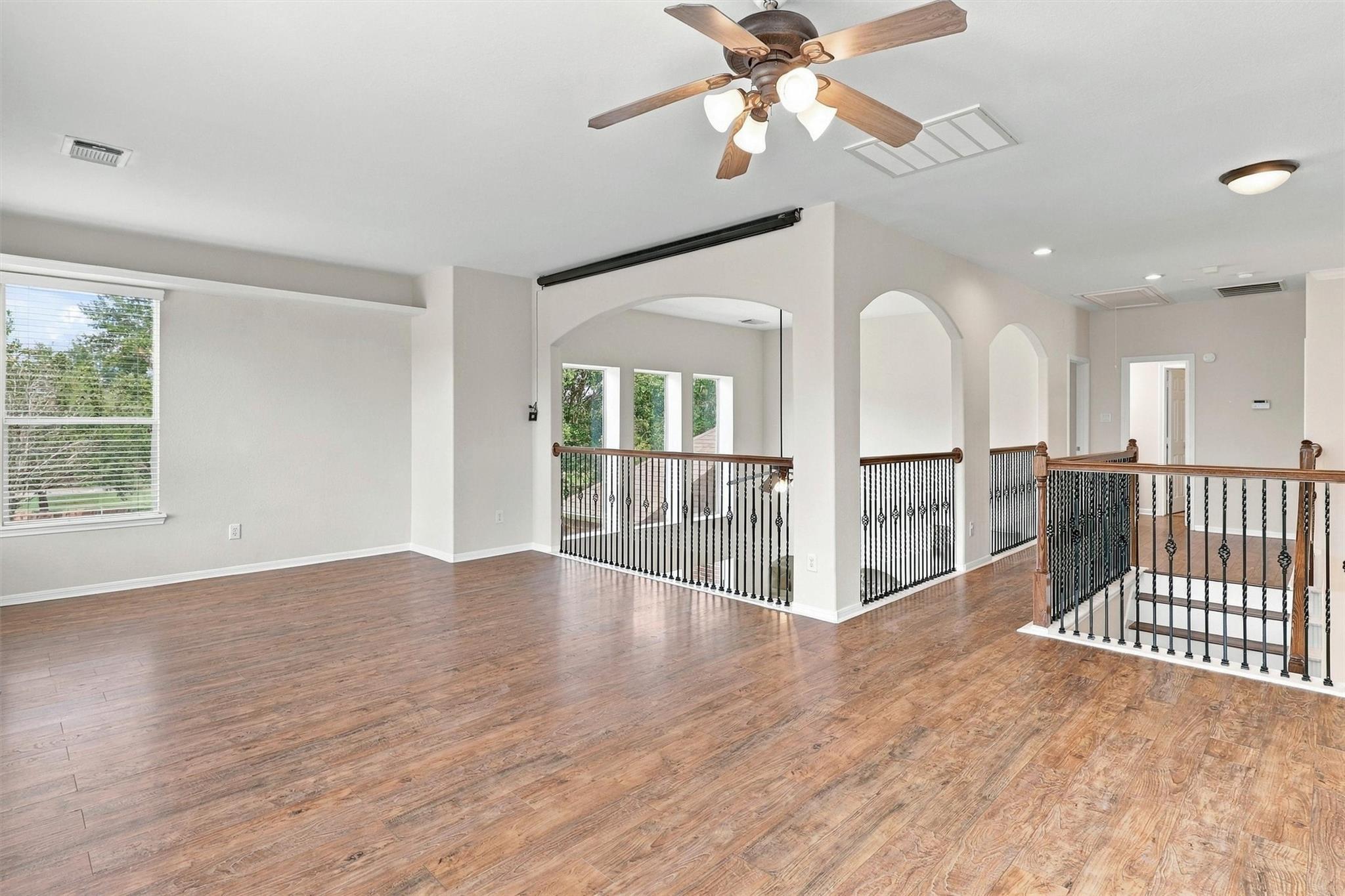 Unfurnished upstairs landing with wood floors, arched openings, and black iron stair railings.
