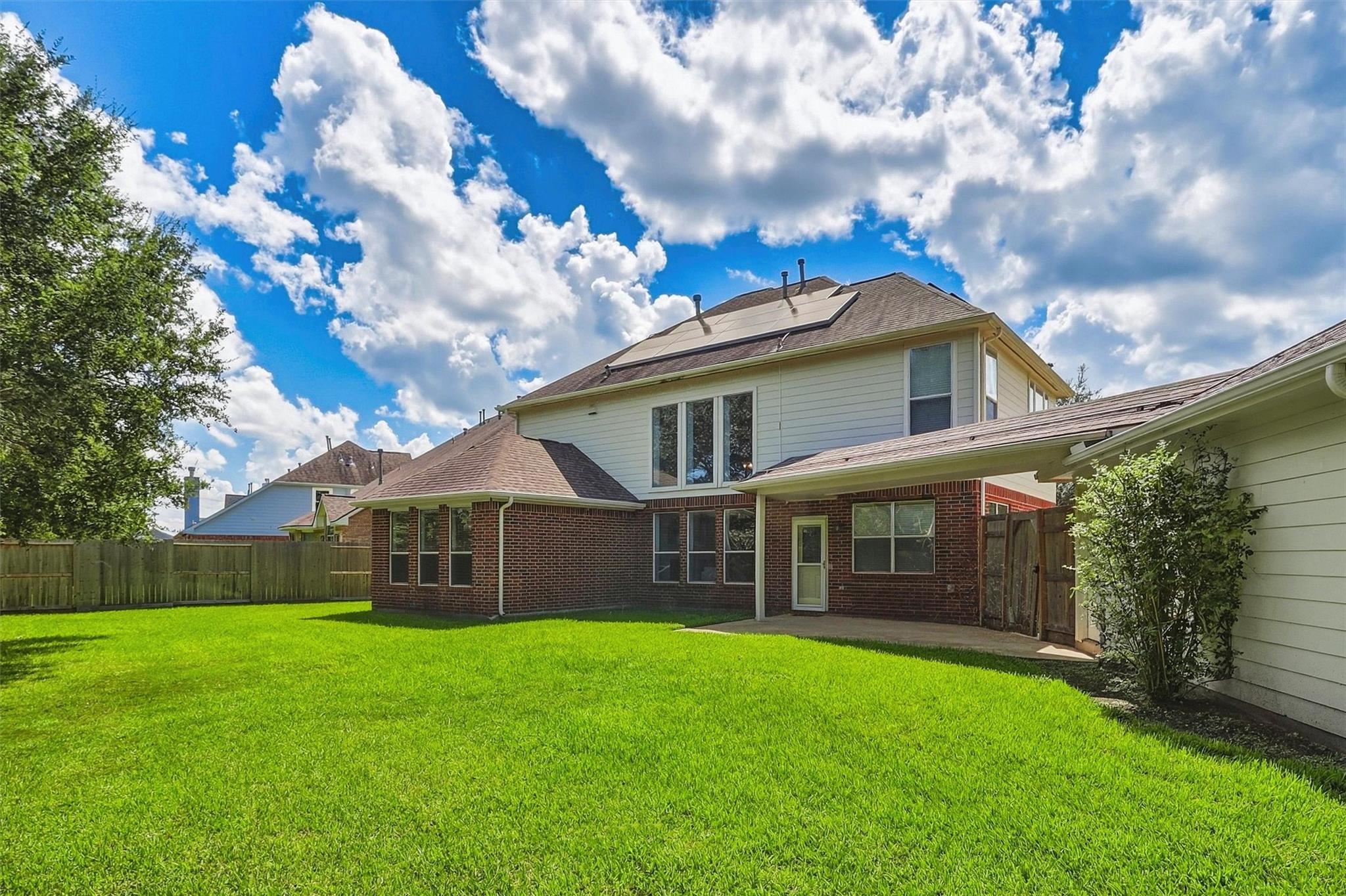 House rear exterior with rooftop solar panels, brick lower level, and a wide fenced lawn.
