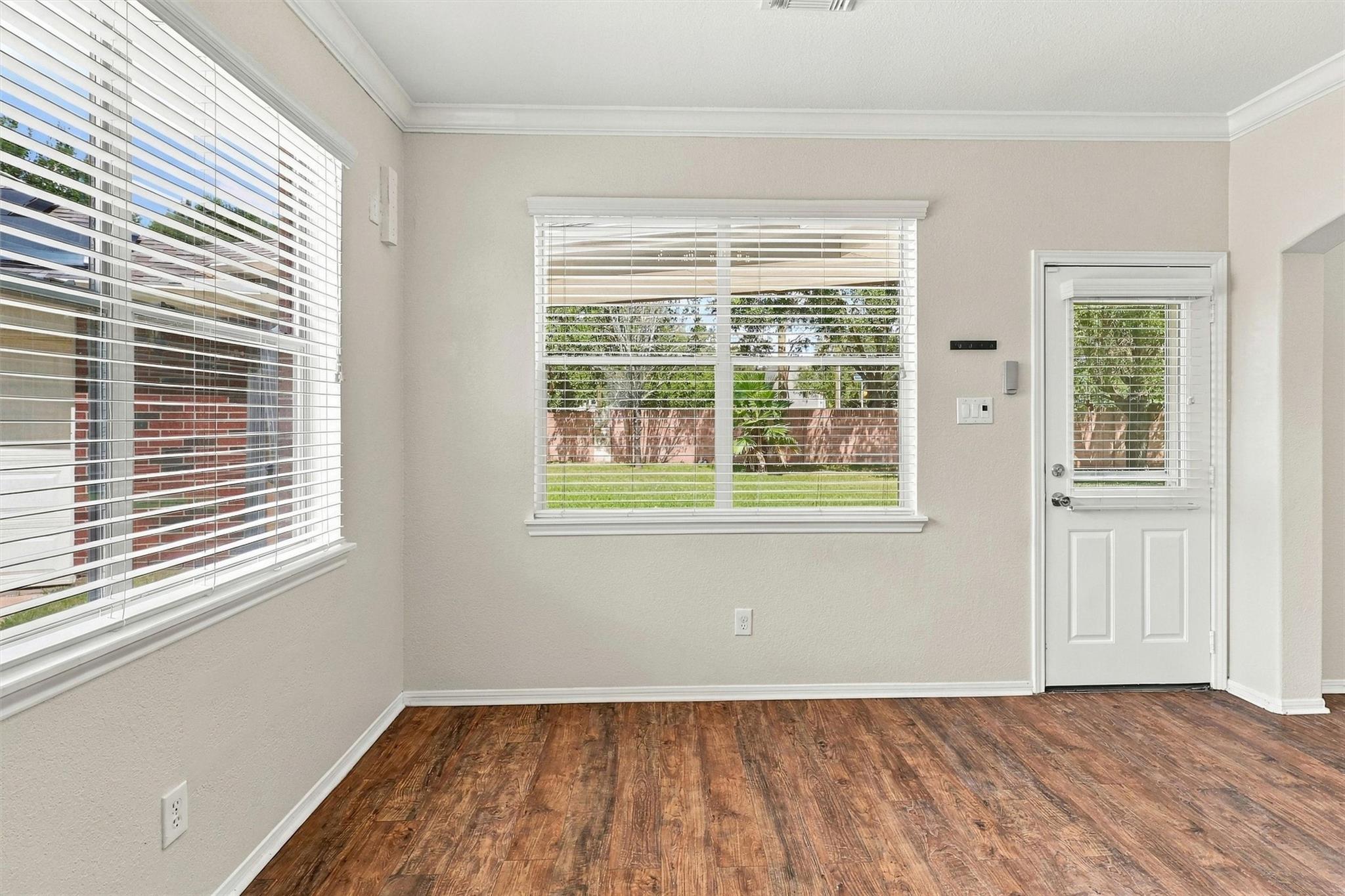 Empty room with wood-look flooring, two windows with blinds, and a white exterior door.