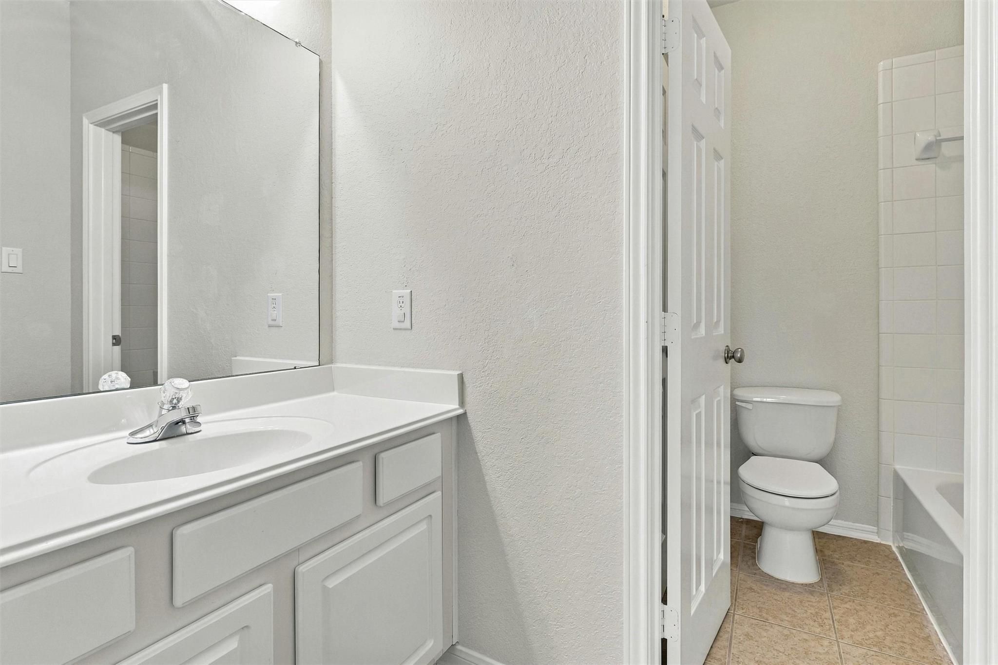 Bathroom with a white vanity and mirror, toilet, and tiled bathtub-shower.