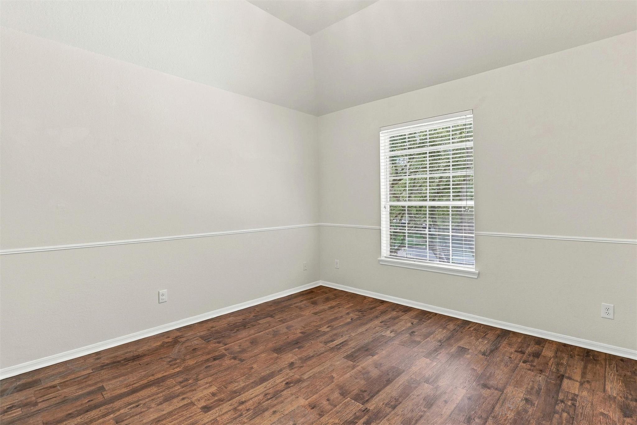 Empty room with dark wood flooring, chair rail molding, and a window with white blinds.