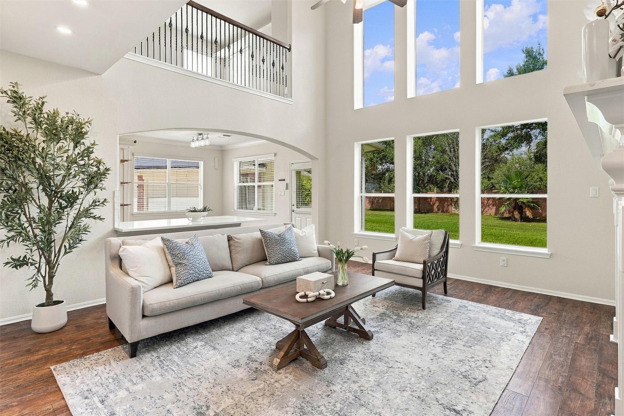Double-height living room with tall backyard-facing windows, a neutral sofa, and a wood coffee table.
