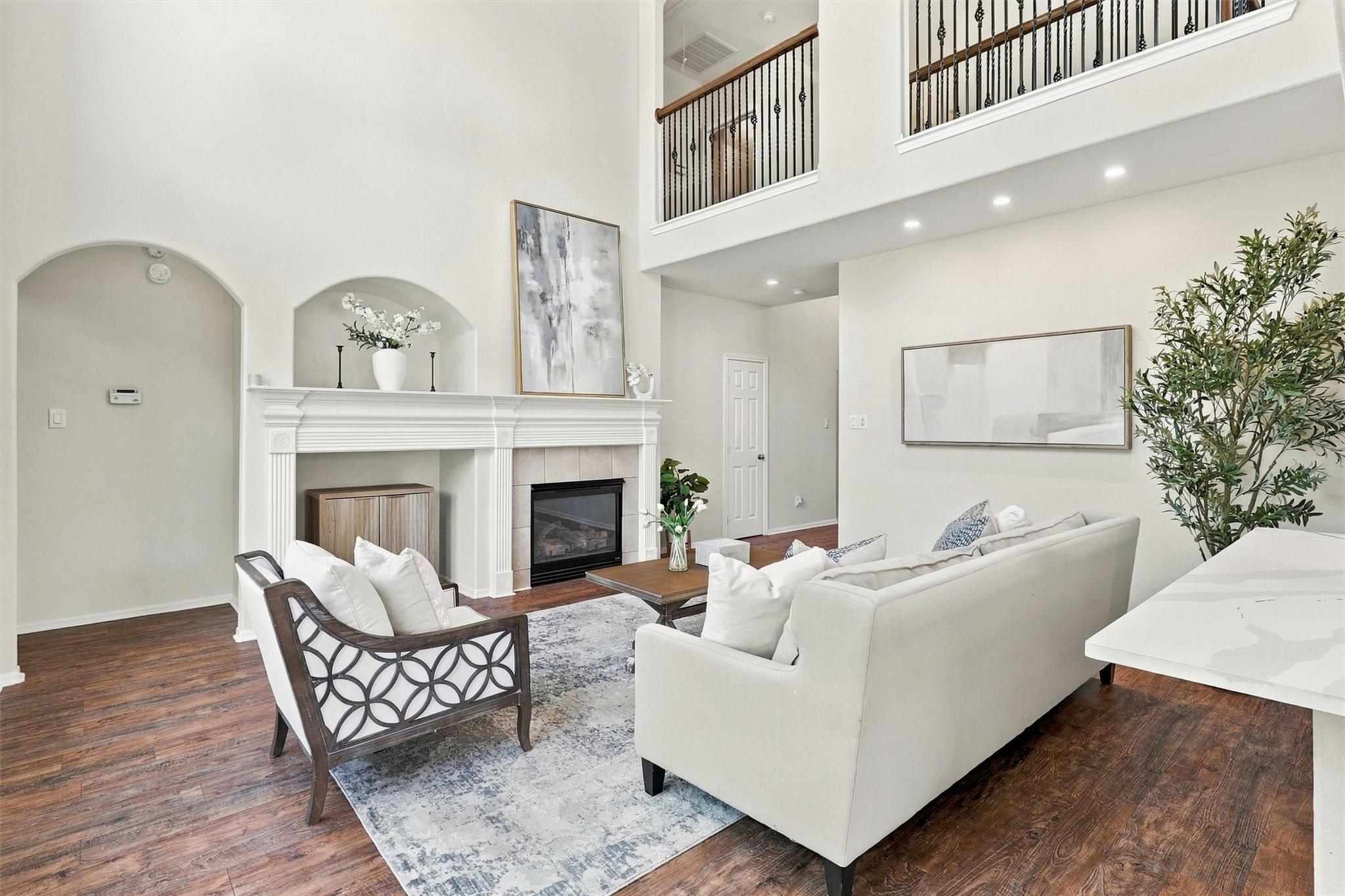 Two-story living room with a white fireplace, upstairs overlook, and neutral seating on dark wood floors.