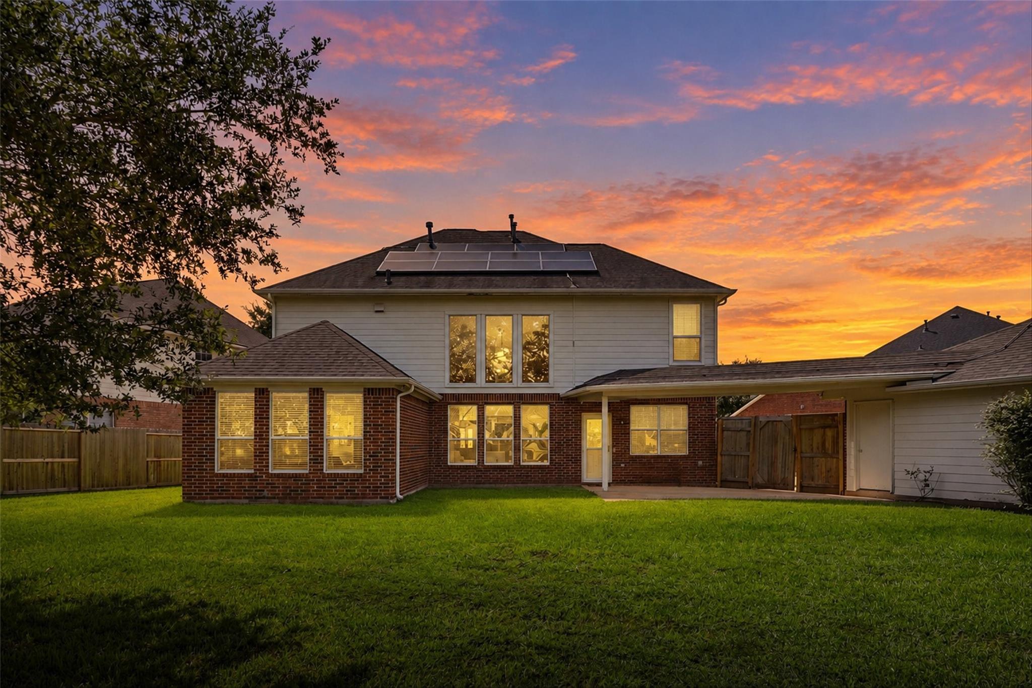 Two-story brick-and-siding home with rooftop solar panels, seen from the lawn at dusk.