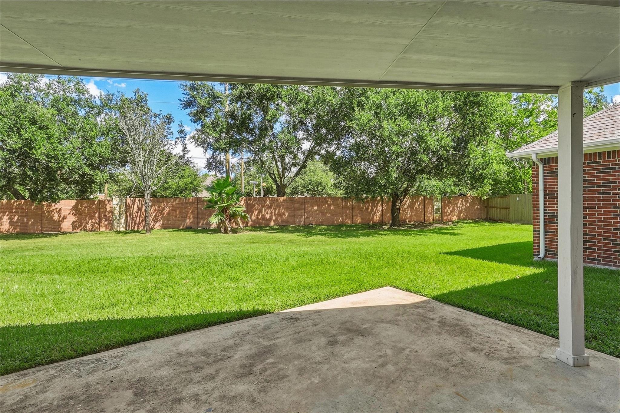 Covered patio overlooking a green backyard with mature trees and a brick privacy fence.