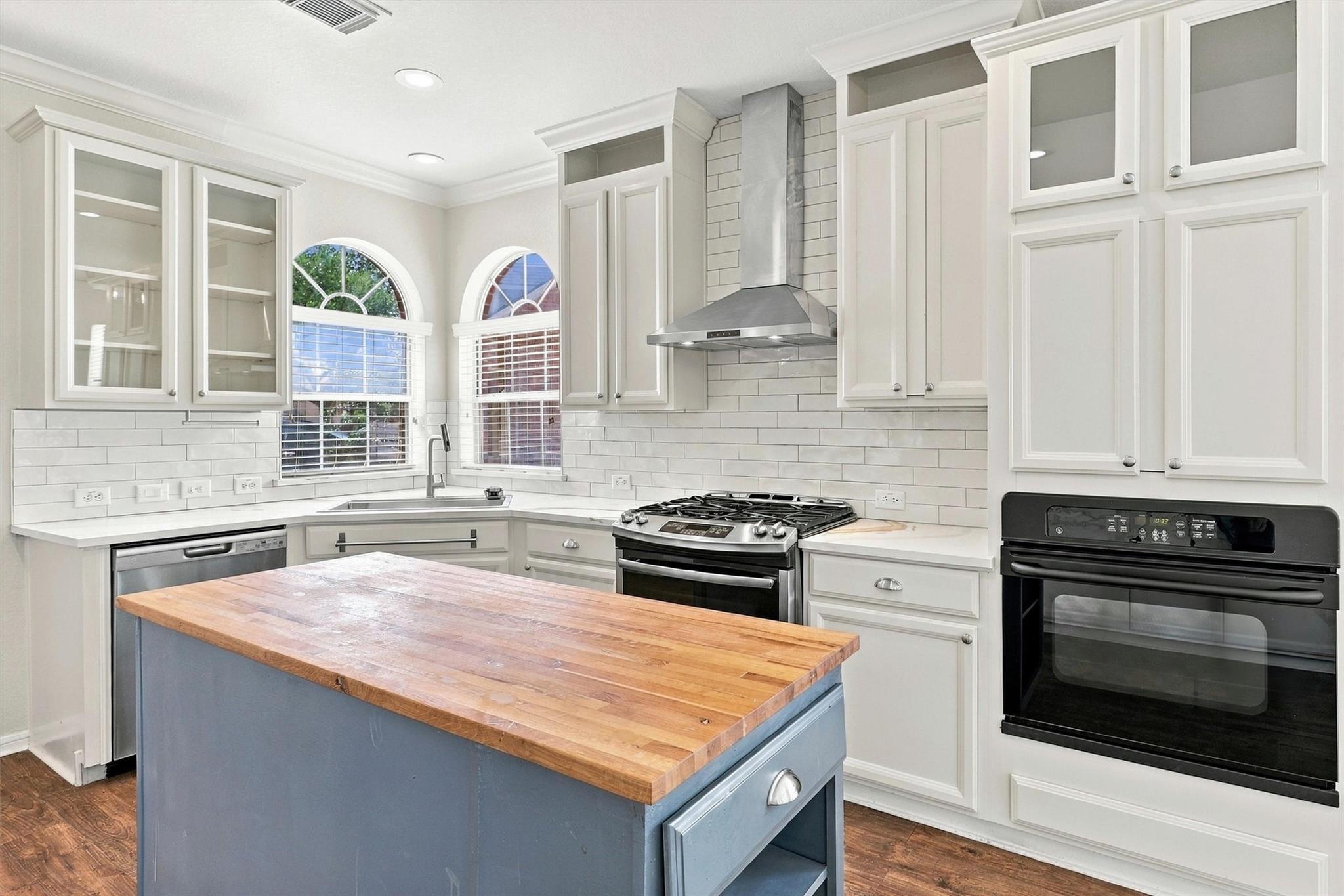 Kitchen with a blue butcher-block island, white cabinets, subway tile, and arched windows.