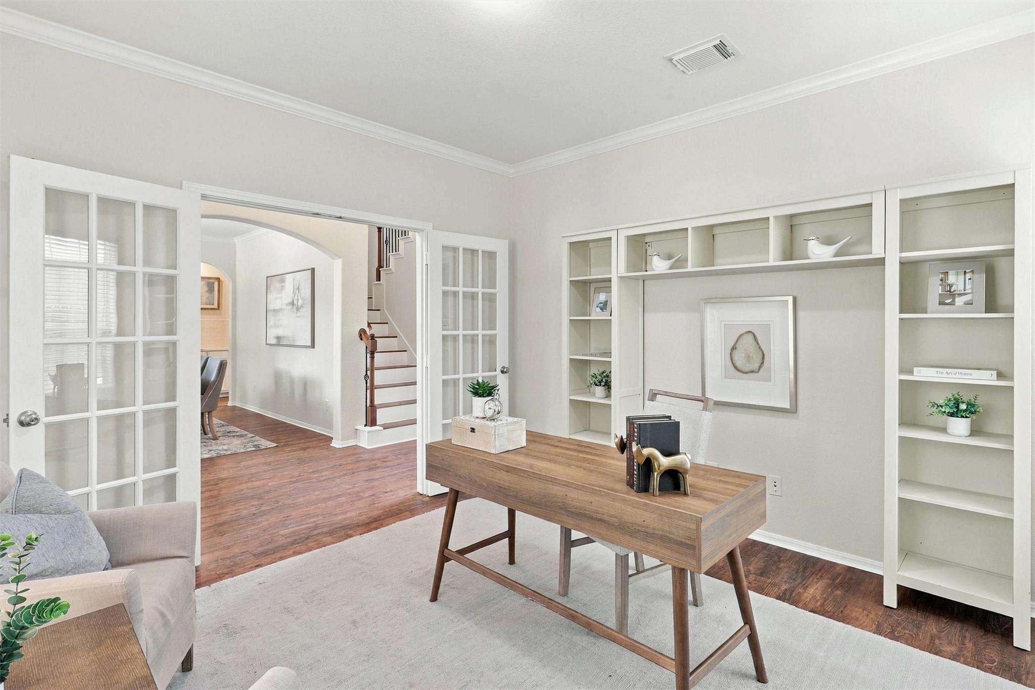Home office with a wooden desk, built-in shelving, and French doors beside the staircase.