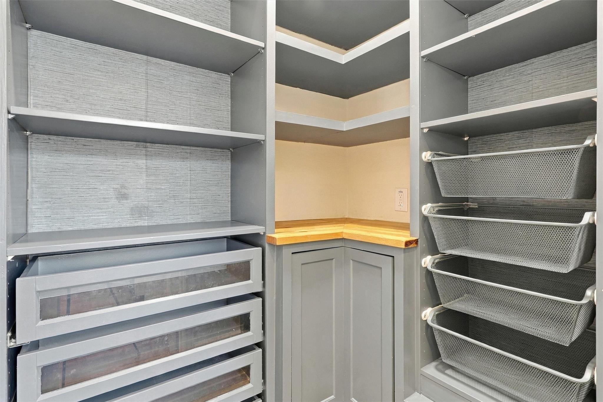 Walk-in closet with gray built-in shelves, clear-front drawers, wire baskets, and a wood corner counter.
