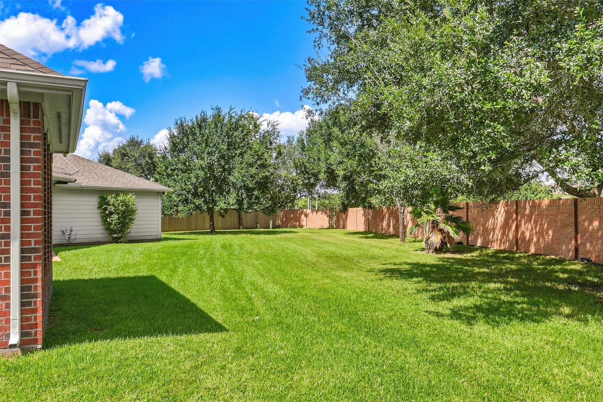 Backyard with a broad green lawn, mature trees, and a brick privacy fence.