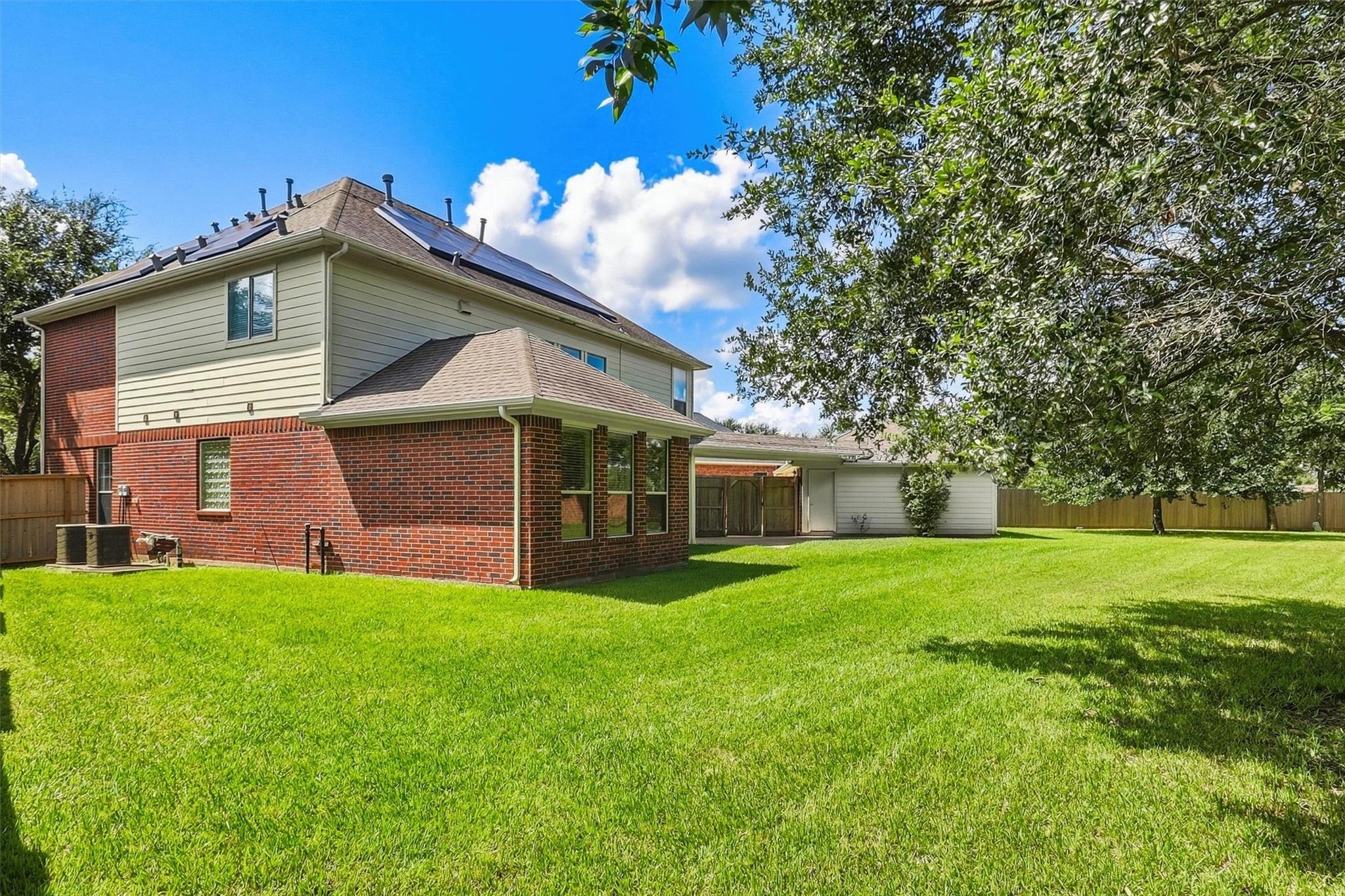 Two-story brick-and-siding home with rooftop solar panels and a broad green backyard.