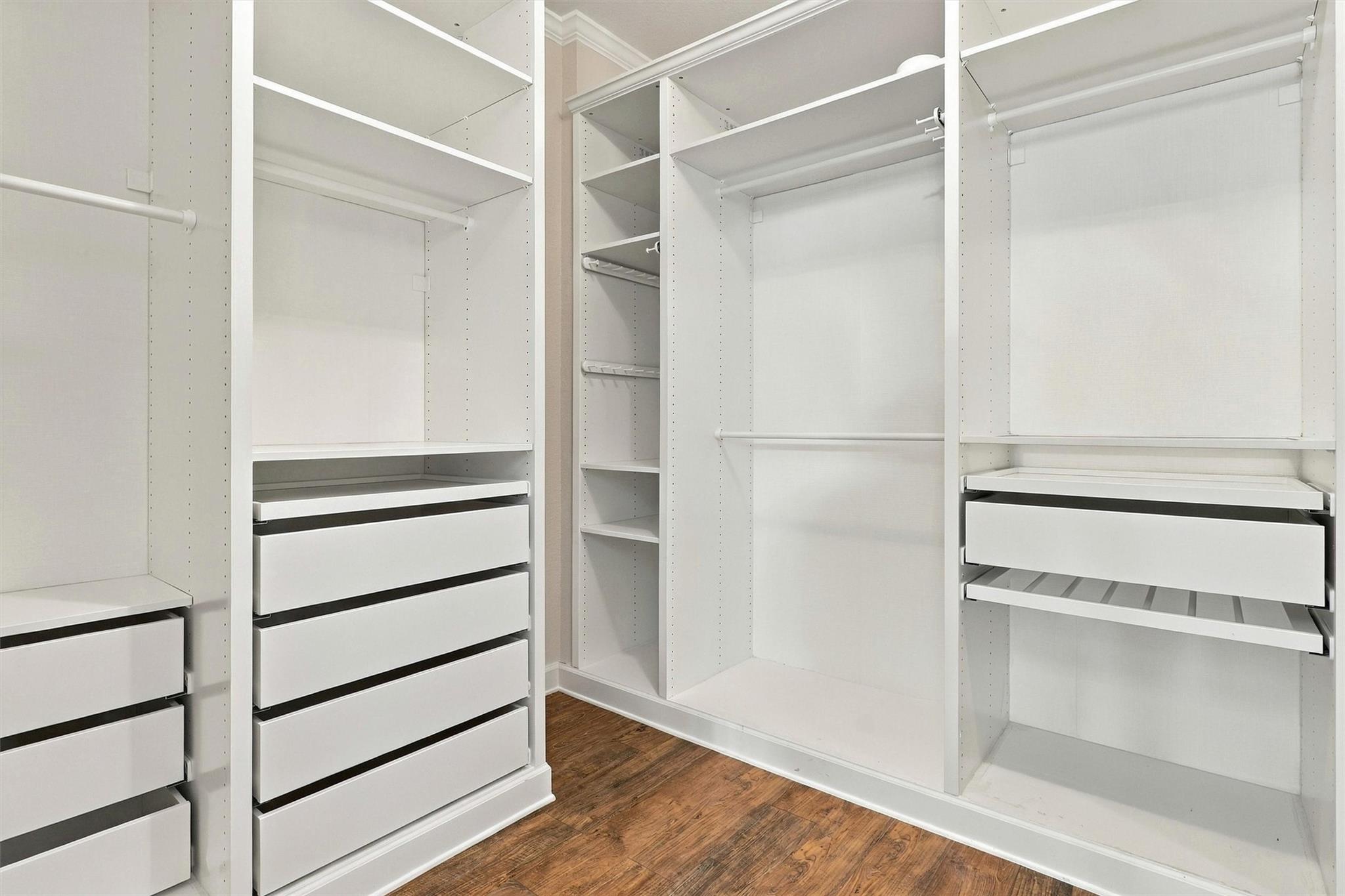 Walk-in closet with white built-in shelving, hanging rods, and wide drawers over a dark wood floor.