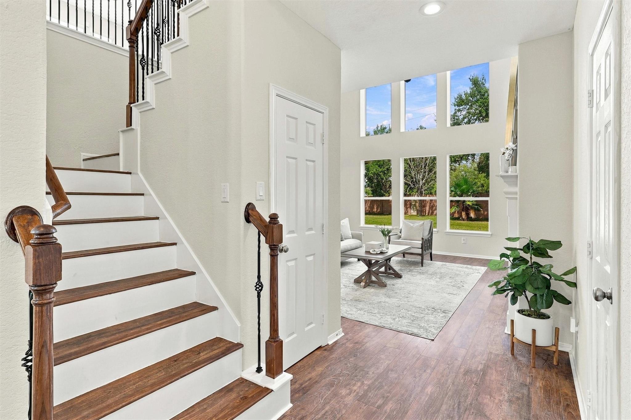 Bright entry foyer with a wood-and-white staircase opening to a sitting area with tall windows.