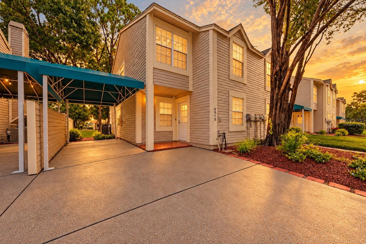 Two-story townhouse exterior with a covered carport and landscaped entry at sunset.