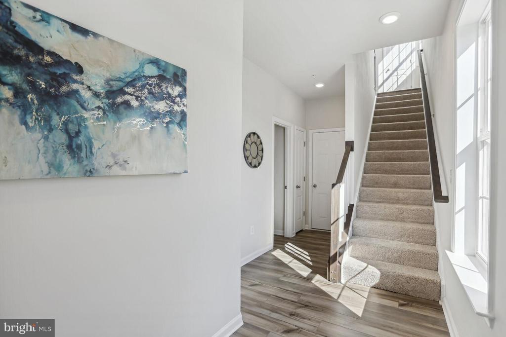 Bright entry hall with a carpeted staircase, tall windows, and blue abstract wall art.
