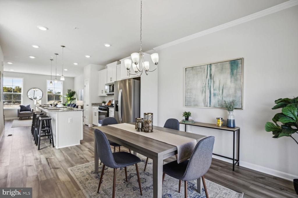 Dining area with a gray table and upholstered chairs beside a bright, open kitchen.