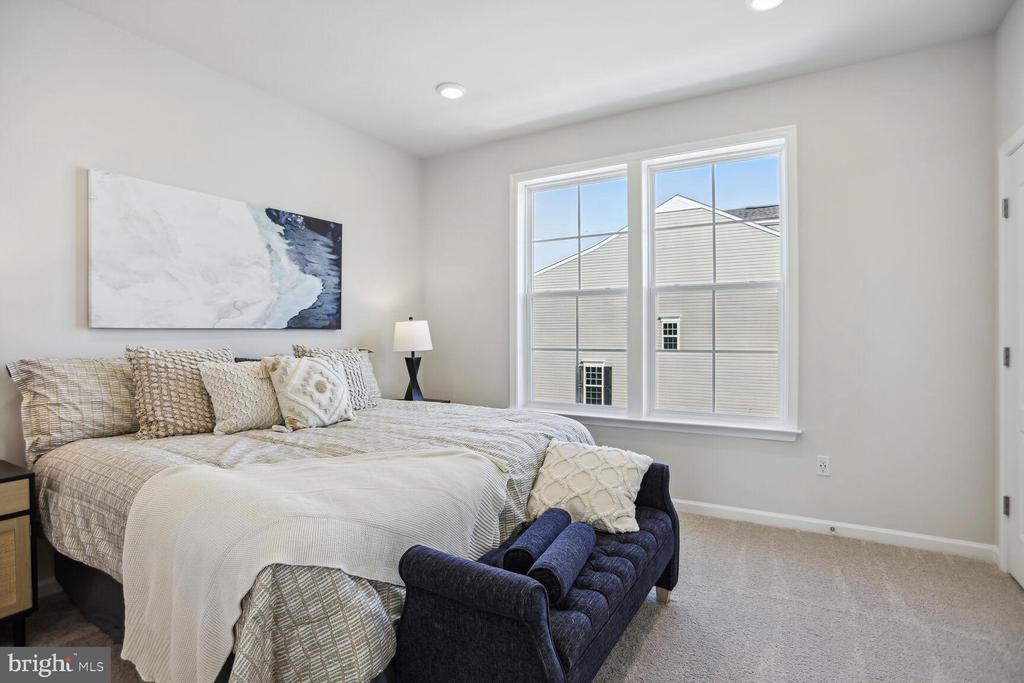 Furnished bedroom with a navy bench, abstract wall art, and two large windows.