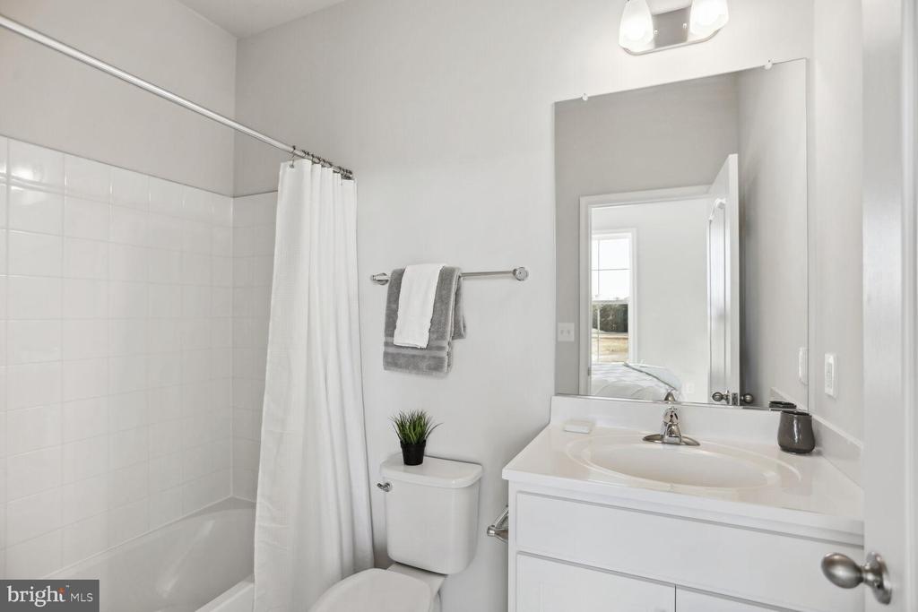 Bright white bathroom with a tiled tub, shower curtain, and vanity topped by a large mirror.