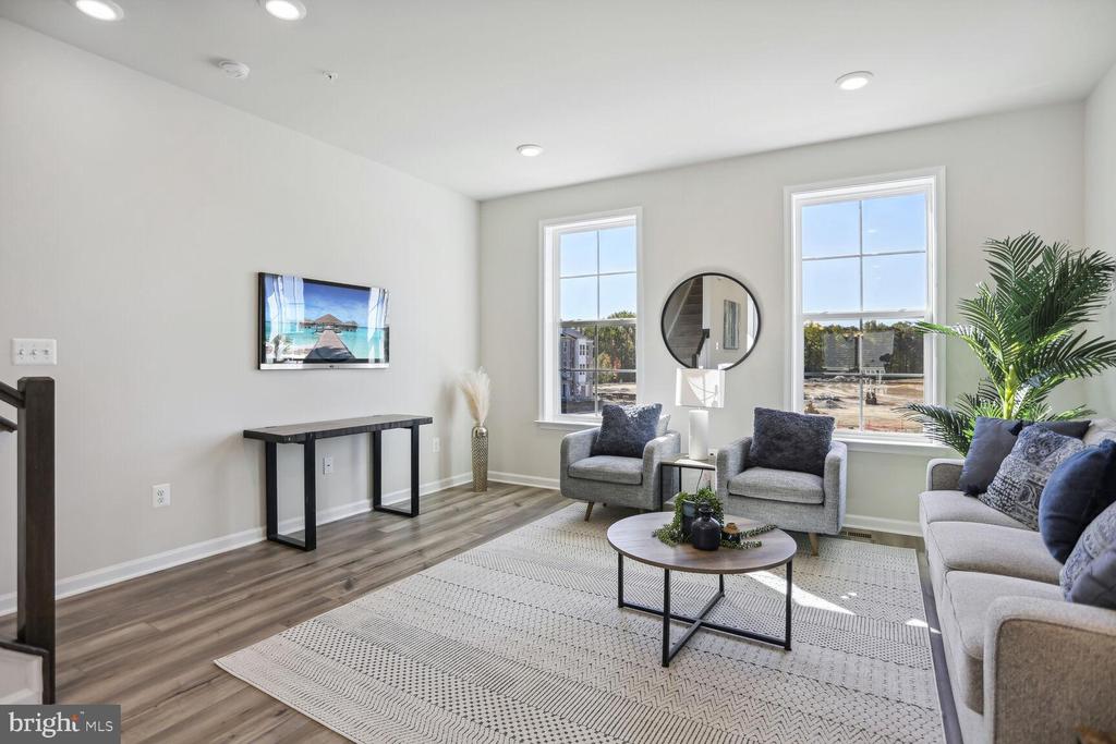 Staged living room with gray seating, a round coffee table, and two large windows.