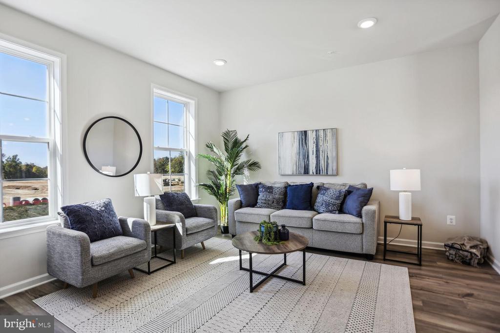 Staged living room with gray seating, a round coffee table, and tall windows overlooking trees.