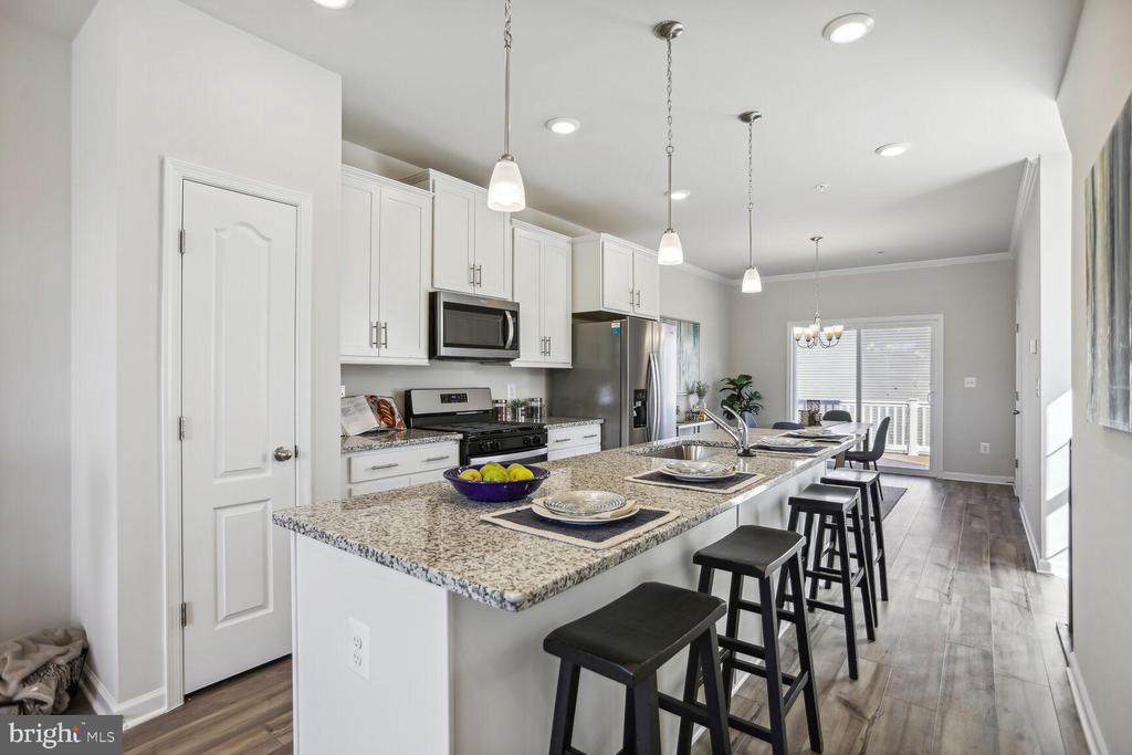 Kitchen with white cabinets, stainless steel appliances, and a granite island lined with black stools.