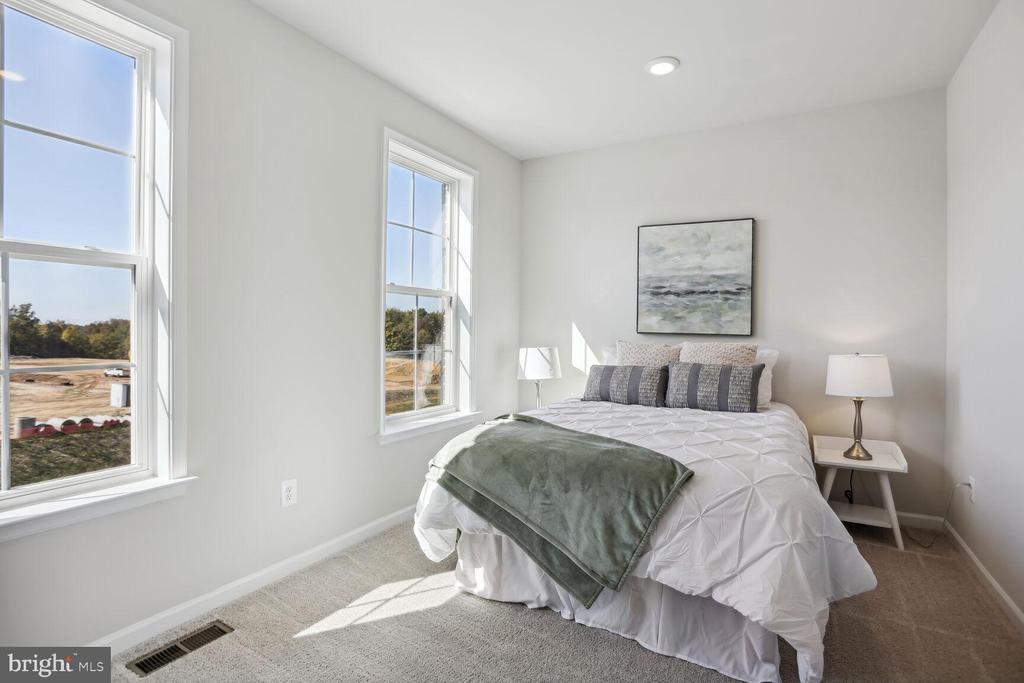 Bright staged bedroom with a white bed, gray-green throw, and two tall windows.