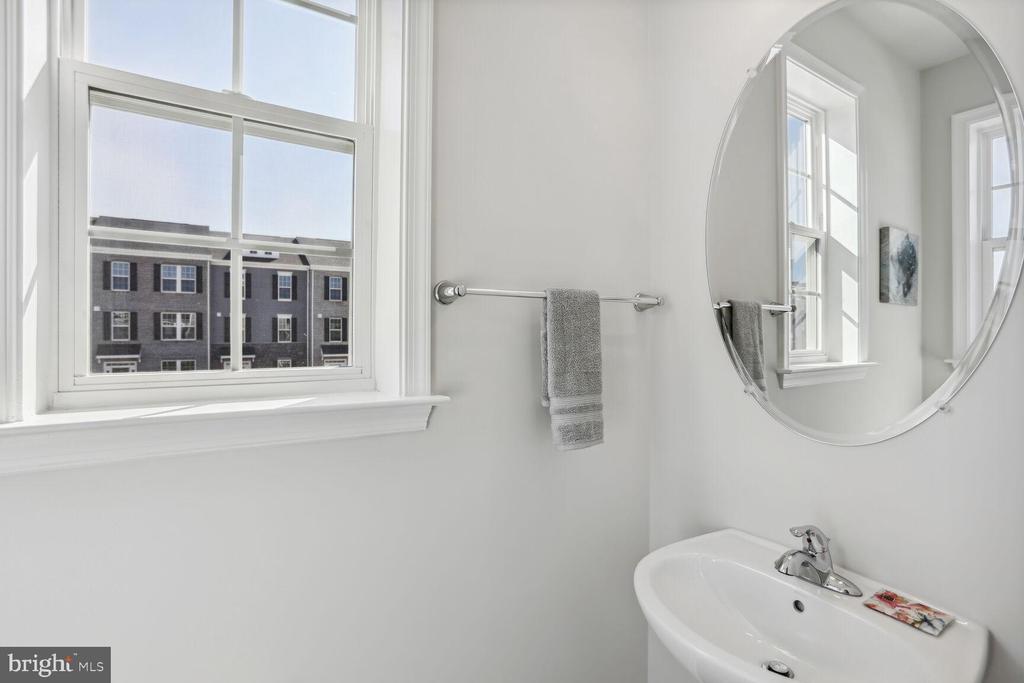 Bright bathroom with a pedestal sink, oval mirror, and window overlooking neighboring townhouses.