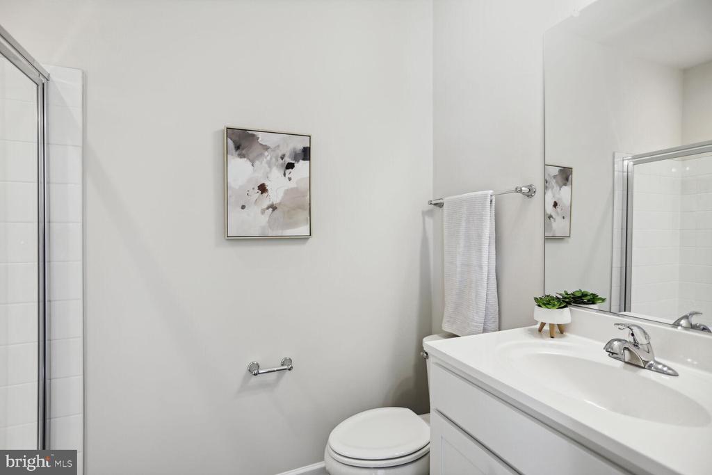 Bright bathroom with white vanity, framed abstract art, toilet, and glass-enclosed shower.