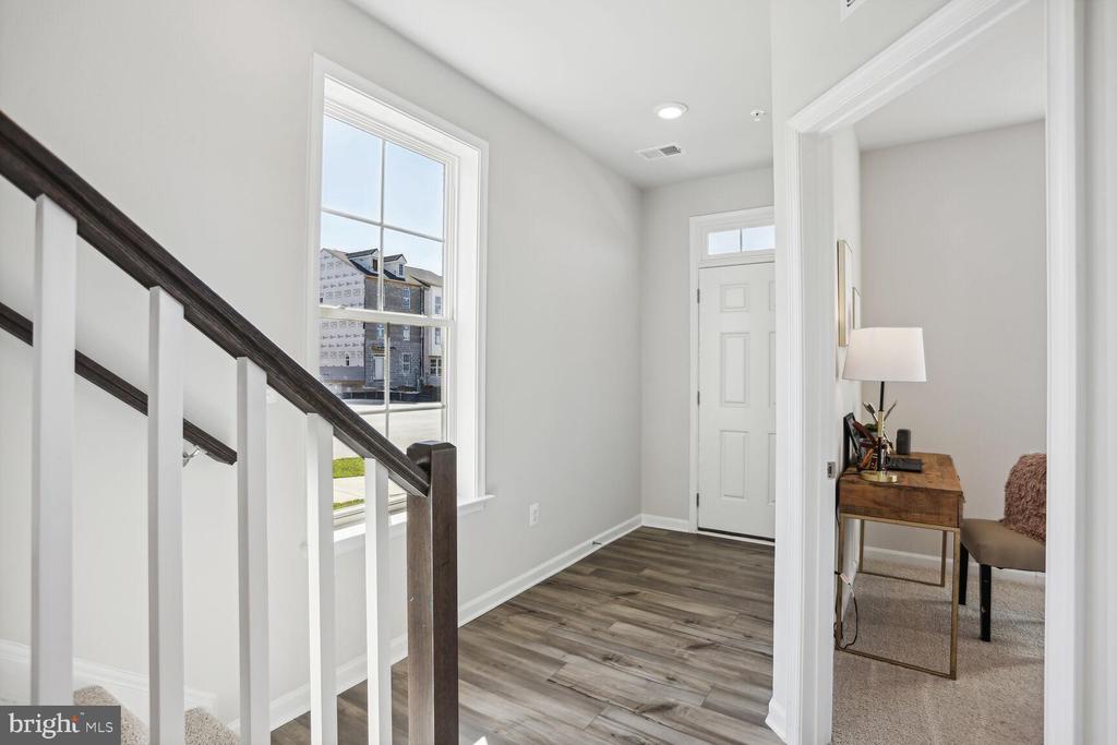 Entry foyer with gray wood-look flooring, a white front door, and staircase with dark handrail.