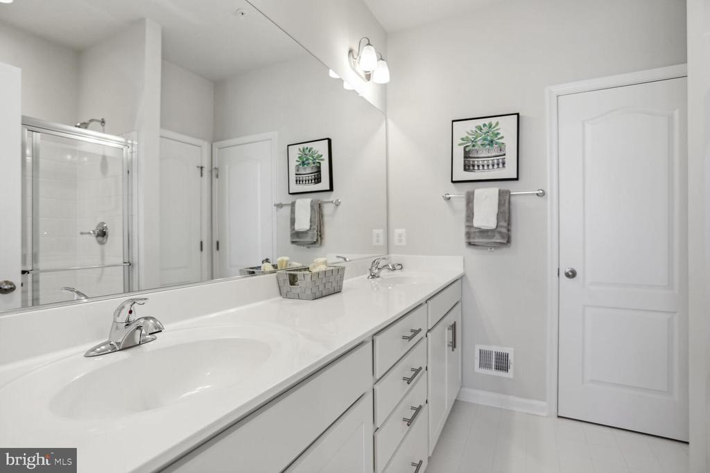 Bright bathroom with a long double vanity, glass shower, and framed plant prints above gray towels.