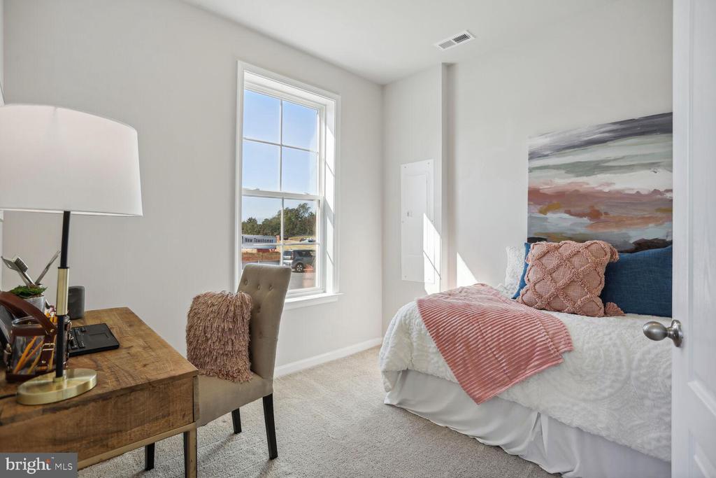 Bright bedroom with a pink striped throw on the bed and a wooden desk beside a tall window.