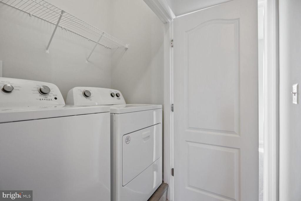 Laundry room with a white washer and dryer beneath a wire storage shelf.