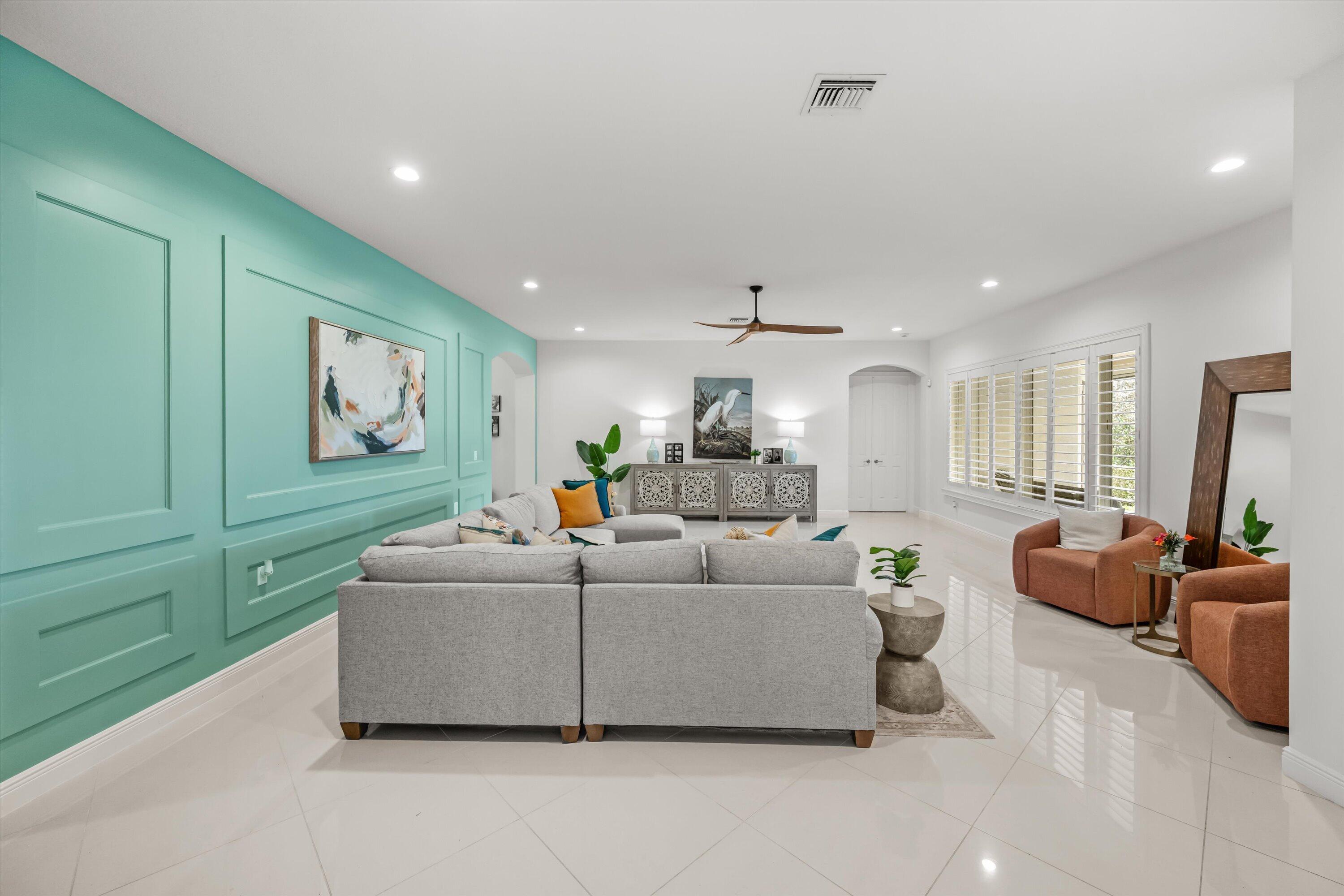 Staged living room with turquoise paneled wall, gray sectional, terracotta armchairs, and glossy tile floors.