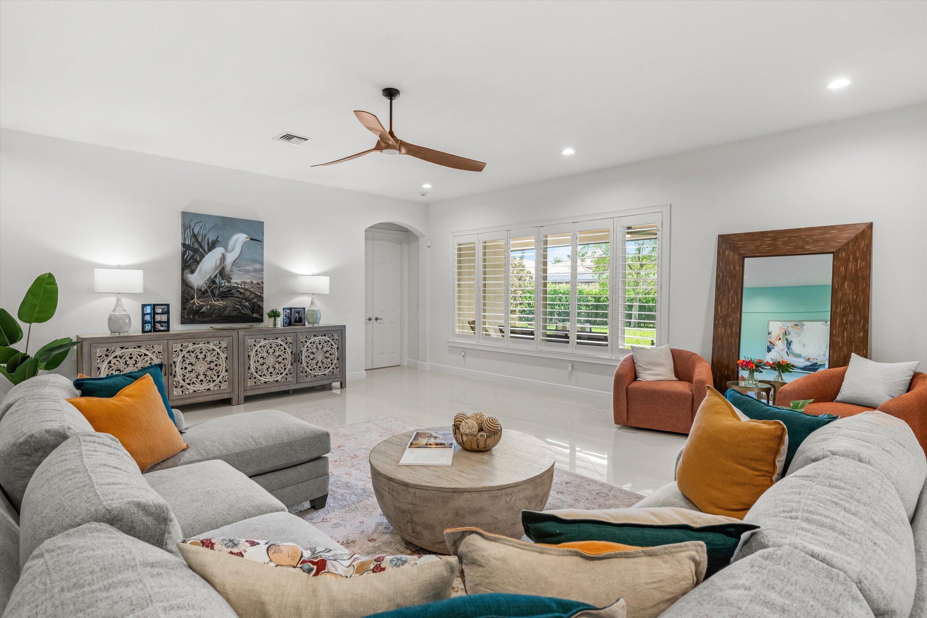 Furnished living room with a gray sectional, rust-colored armchairs, shuttered windows, and a carved sideboard.