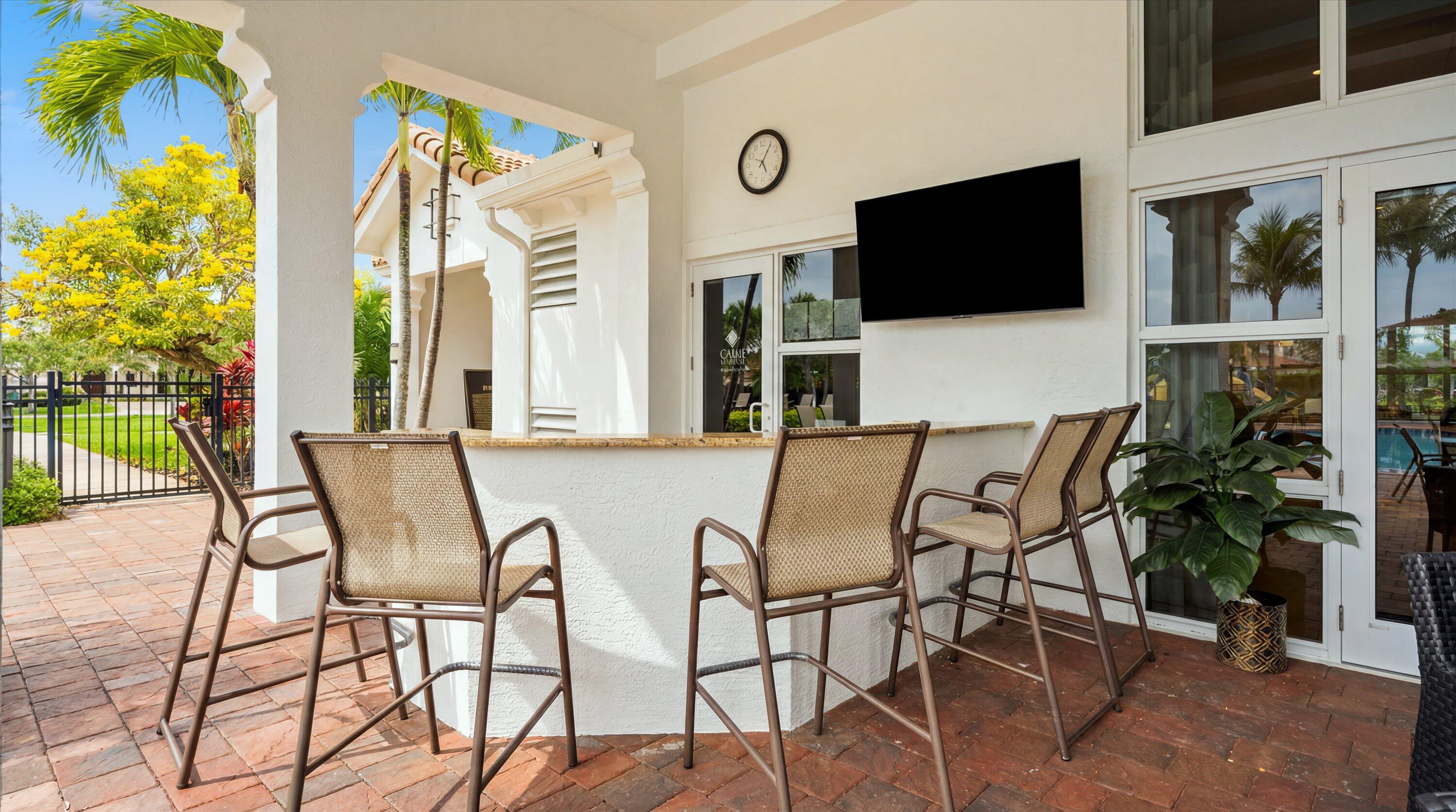 Covered patio with wicker bar stools, brick pavers, and a wall-mounted television.