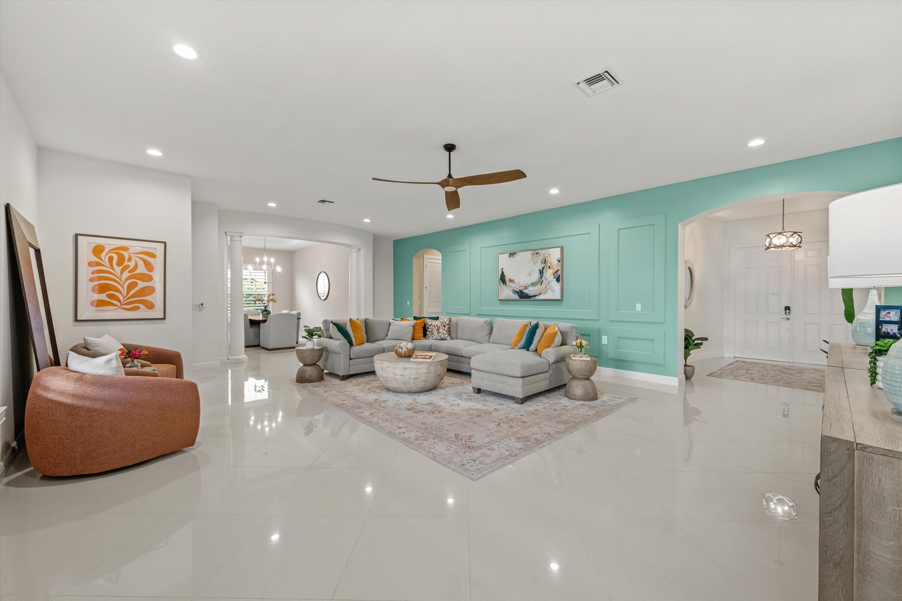 Staged living room with a gray sectional, turquoise paneled wall, rust-colored chairs, and glossy tile floors.