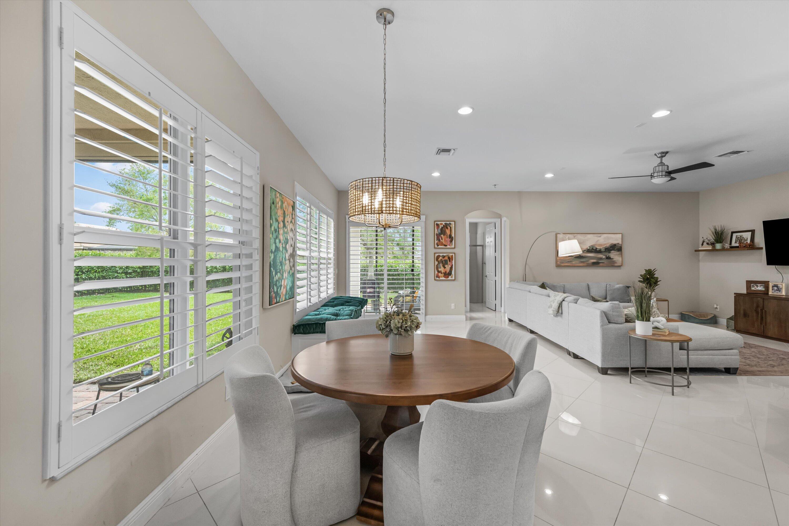 Open-plan living and dining room with plantation shutters, a round wood table, and a gray sectional.