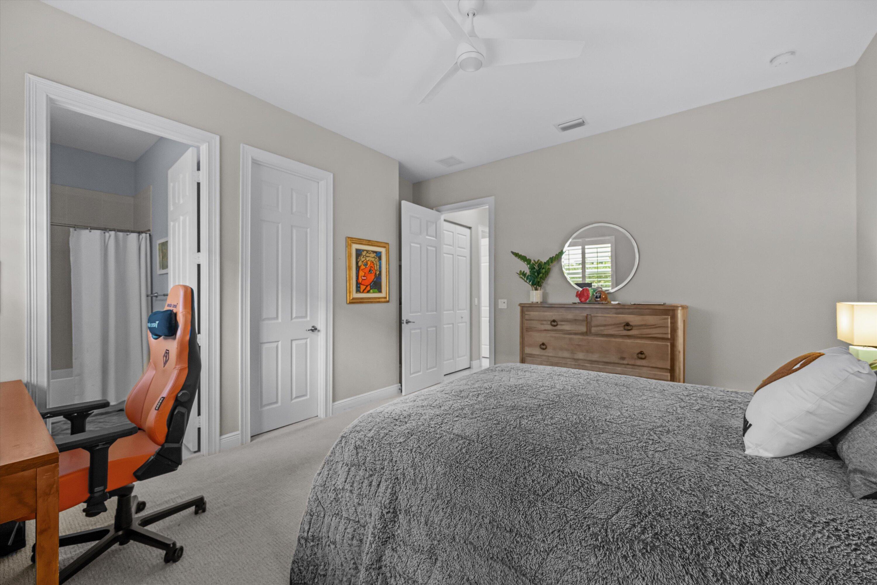 Furnished bedroom with a gray bedspread, wooden dresser, and orange gaming chair beside the bathroom doorway.