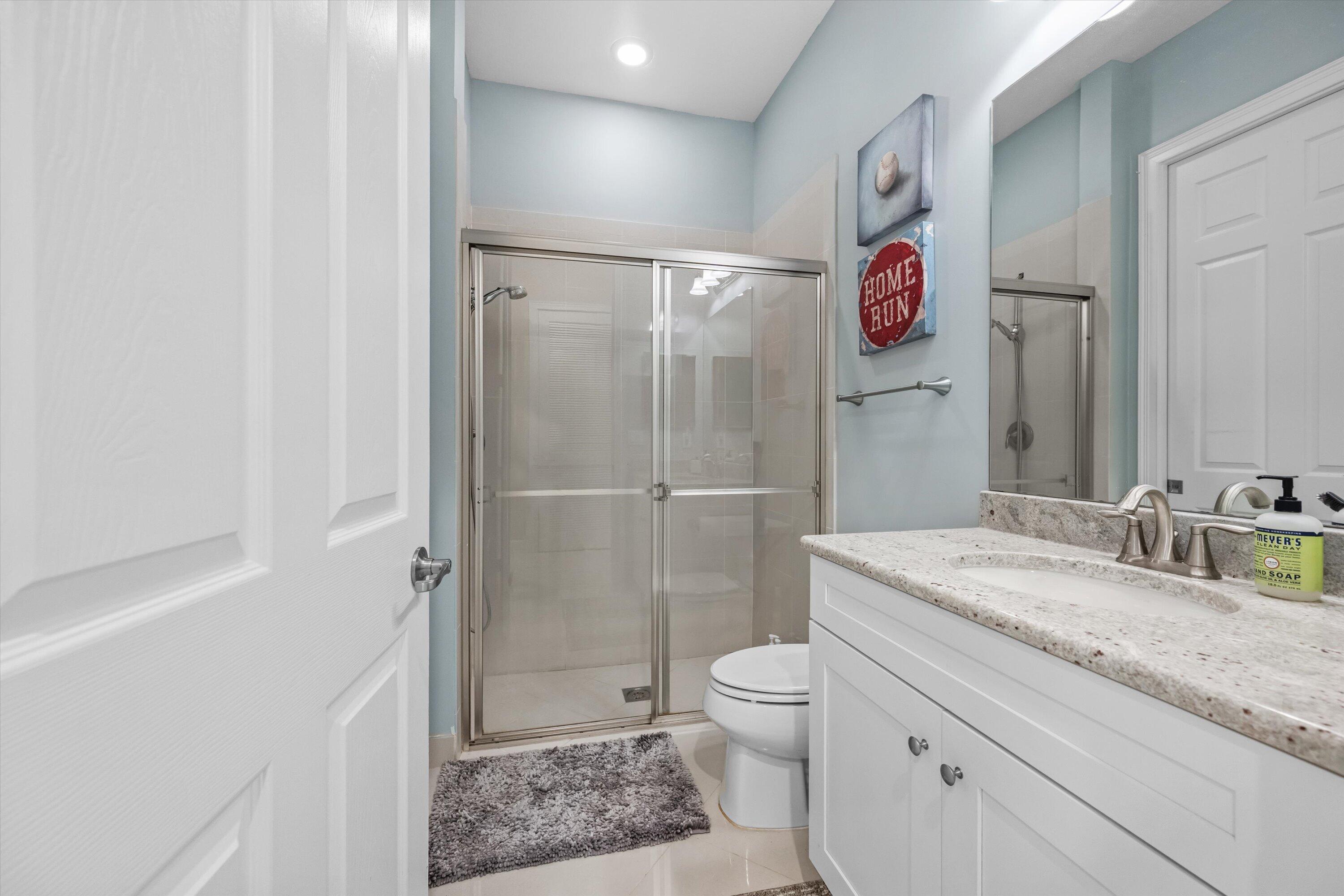 Bathroom with glass-enclosed shower, white vanity, stone countertop, and blue walls.