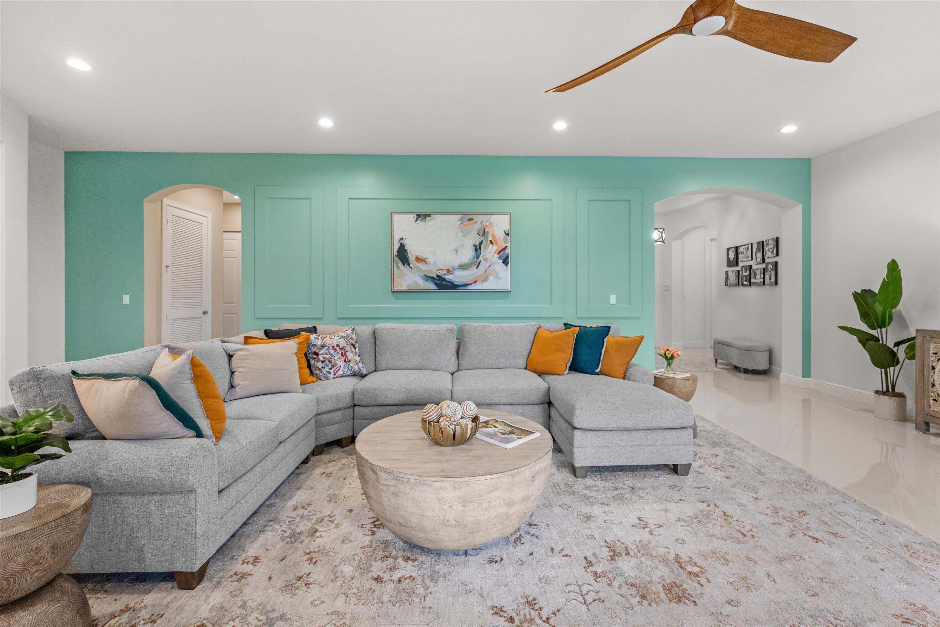 Staged living room with a gray sectional, round coffee table, and turquoise paneled accent wall.