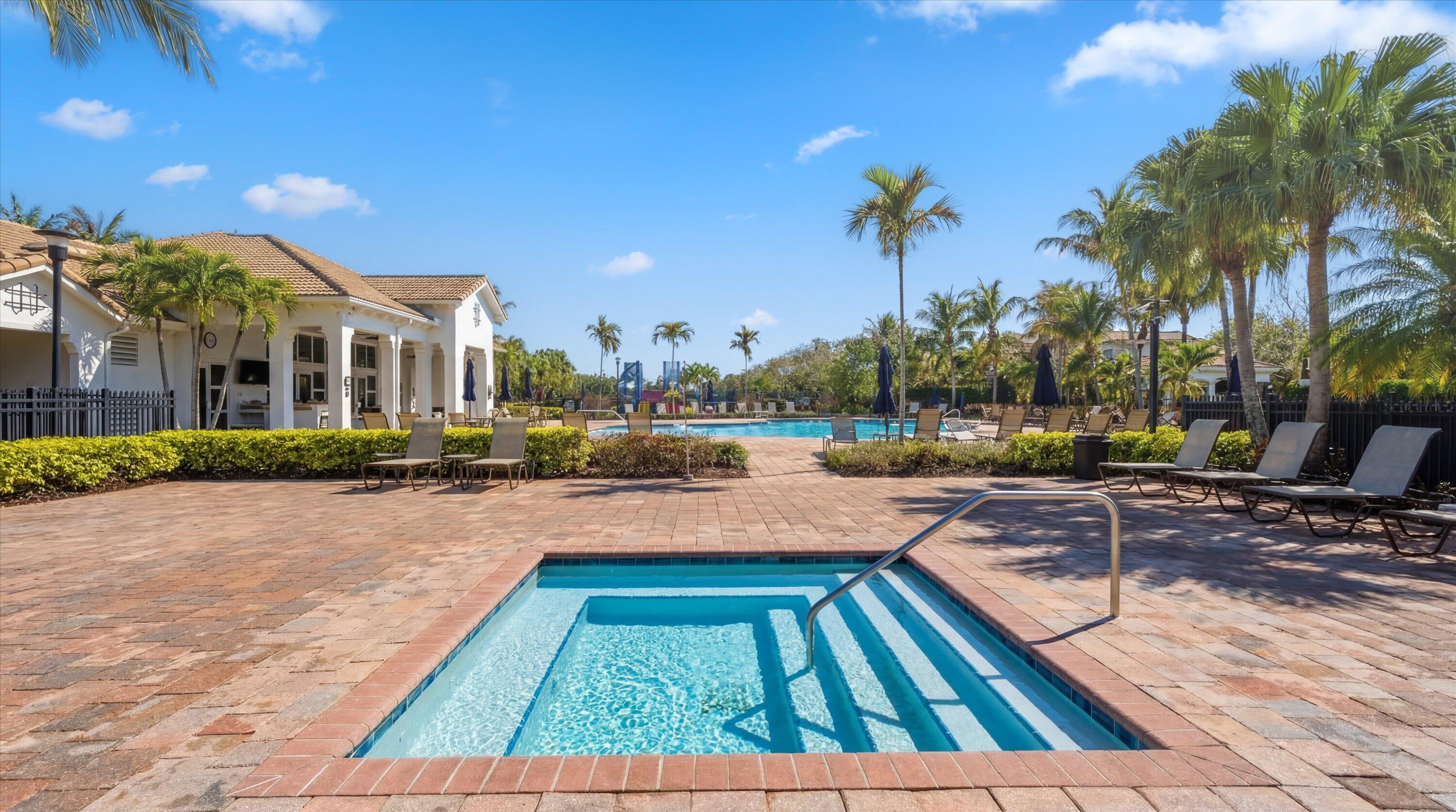 Outdoor pool with a shallow-entry section, palm trees, lounge chairs, and a white clubhouse.