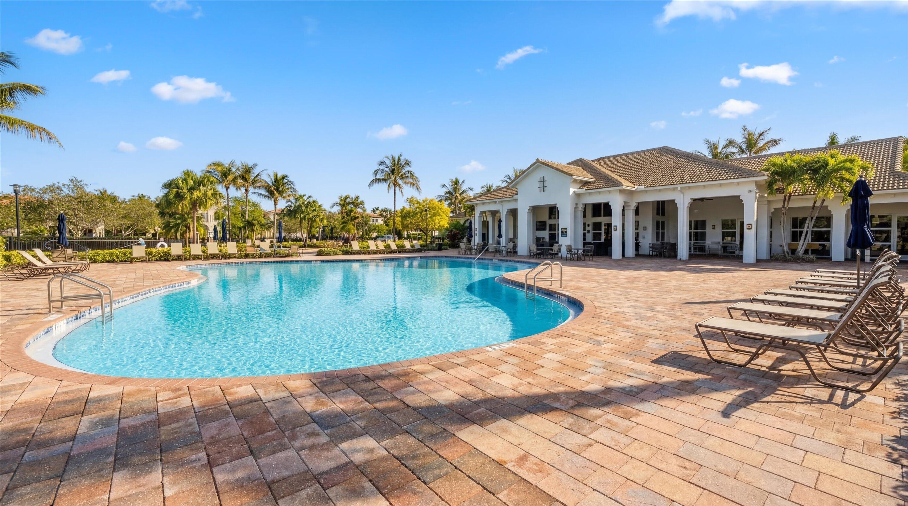 Community swimming pool beside a clubhouse, with palm trees and rows of lounge chairs.