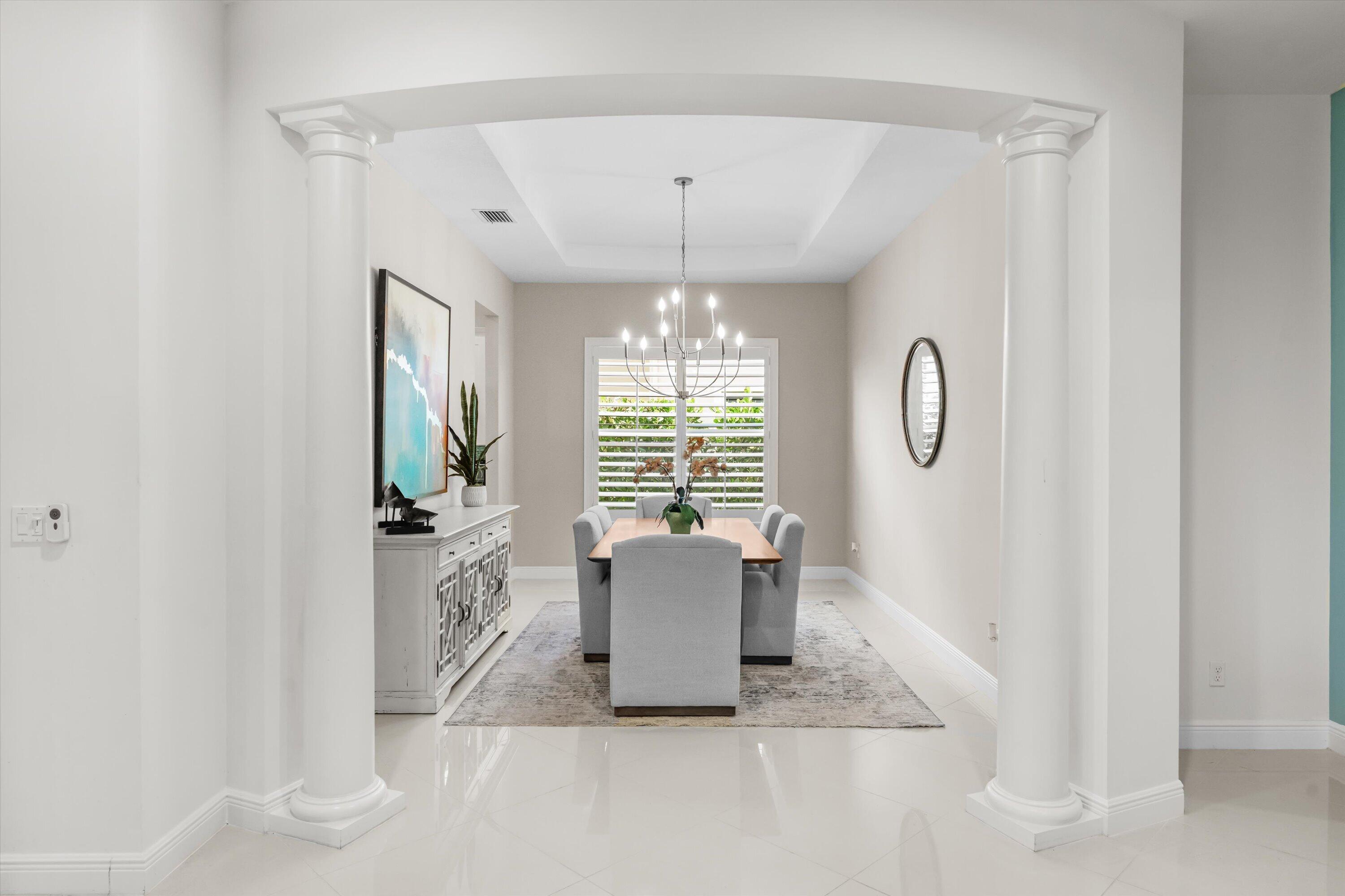 Dining room with a chandelier, gray upholstered chairs, and plantation shutters.