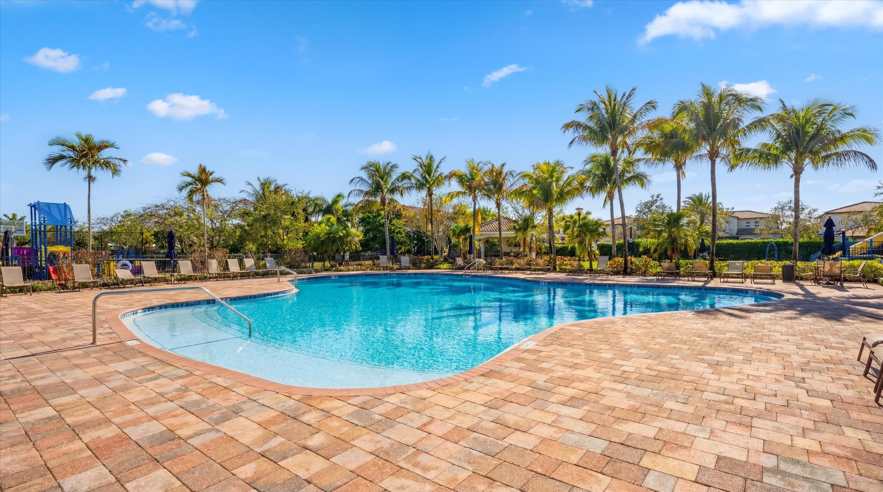 Community pool with a shallow entry, broad paver deck, palm trees, and lounge chairs.