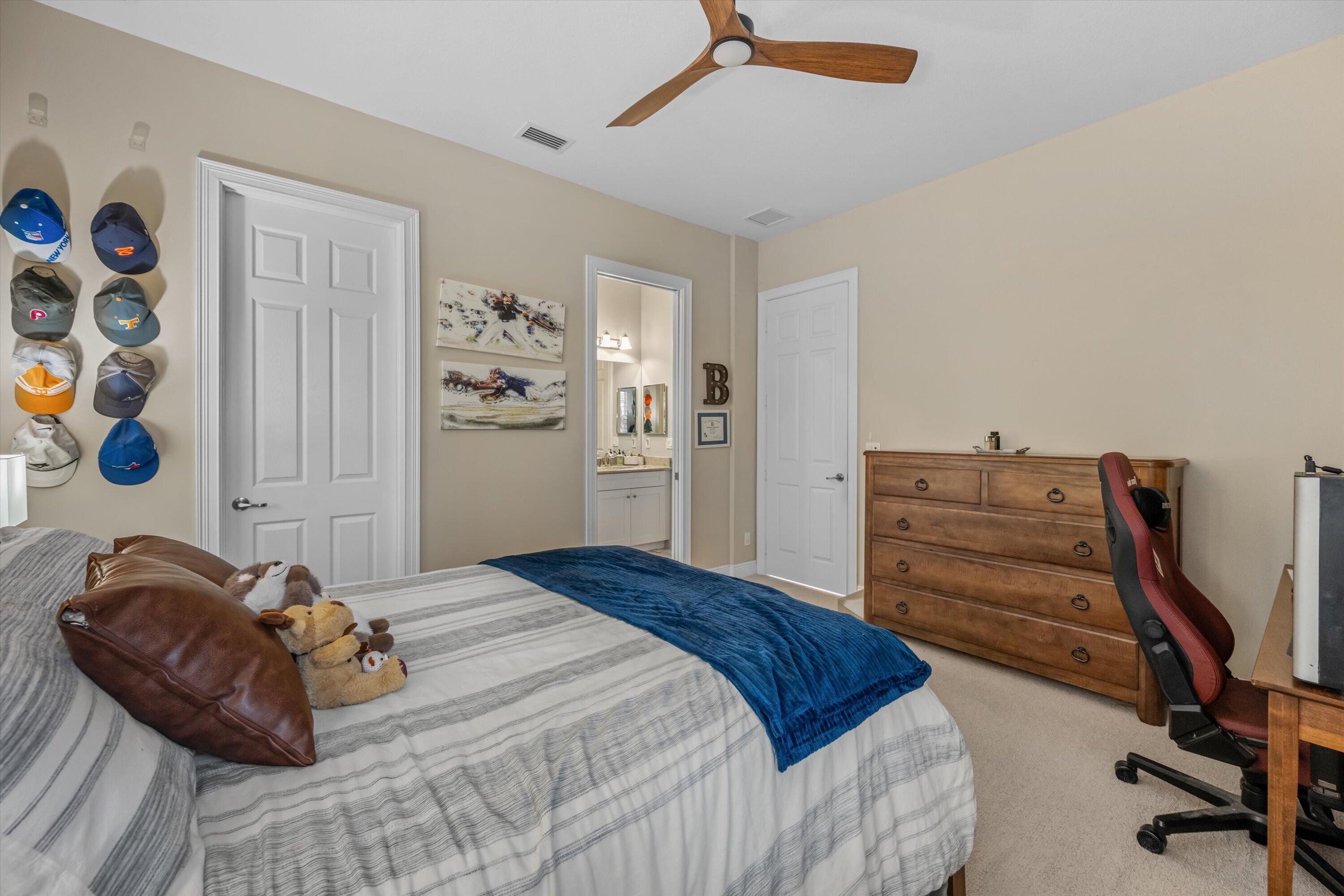 Bedroom with gray striped bedding, a blue throw, wall-mounted baseball caps, and a wooden dresser.