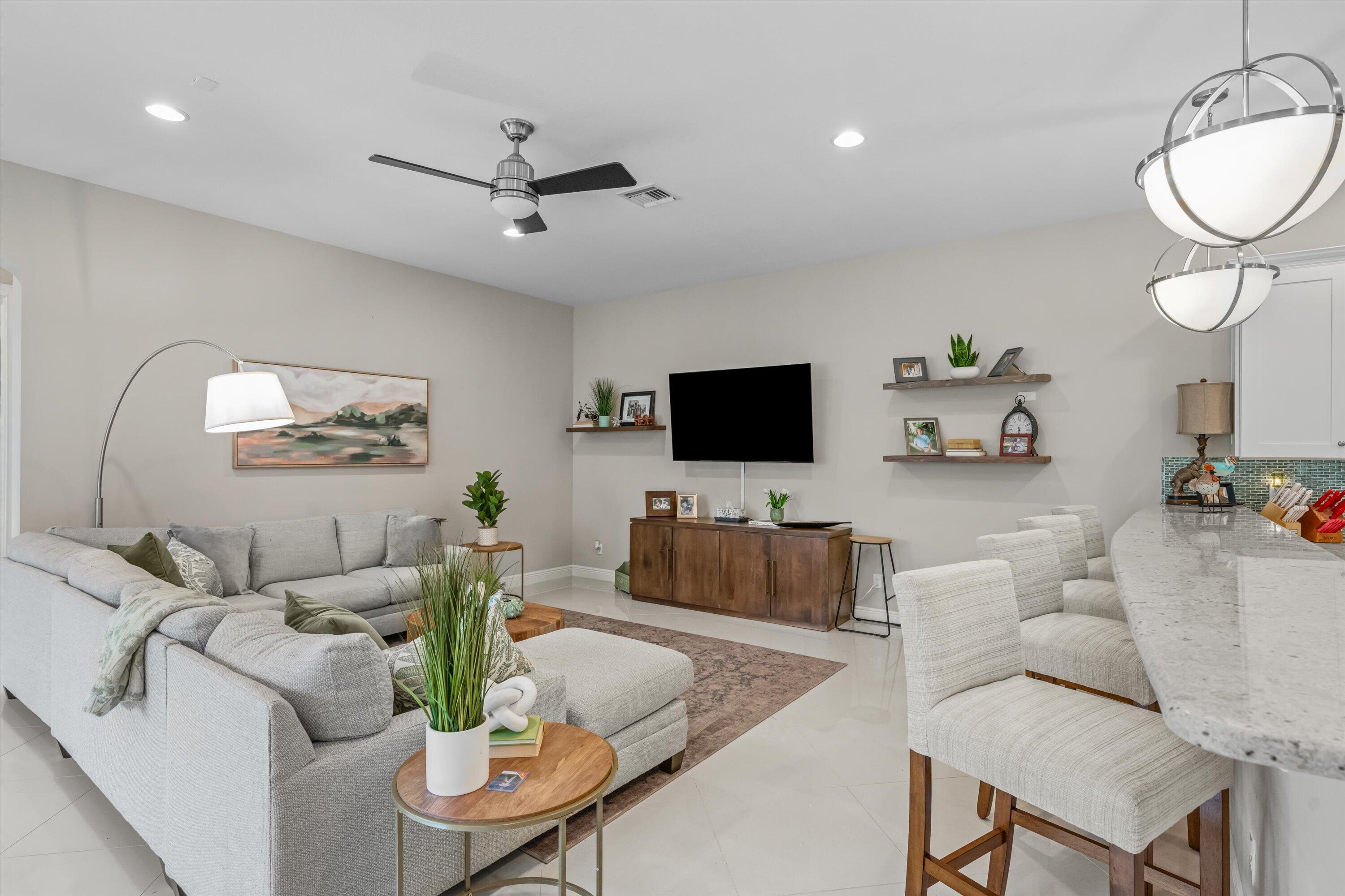 Open-plan living room and dining area with gray sectional, wall-mounted TV, and kitchen island.